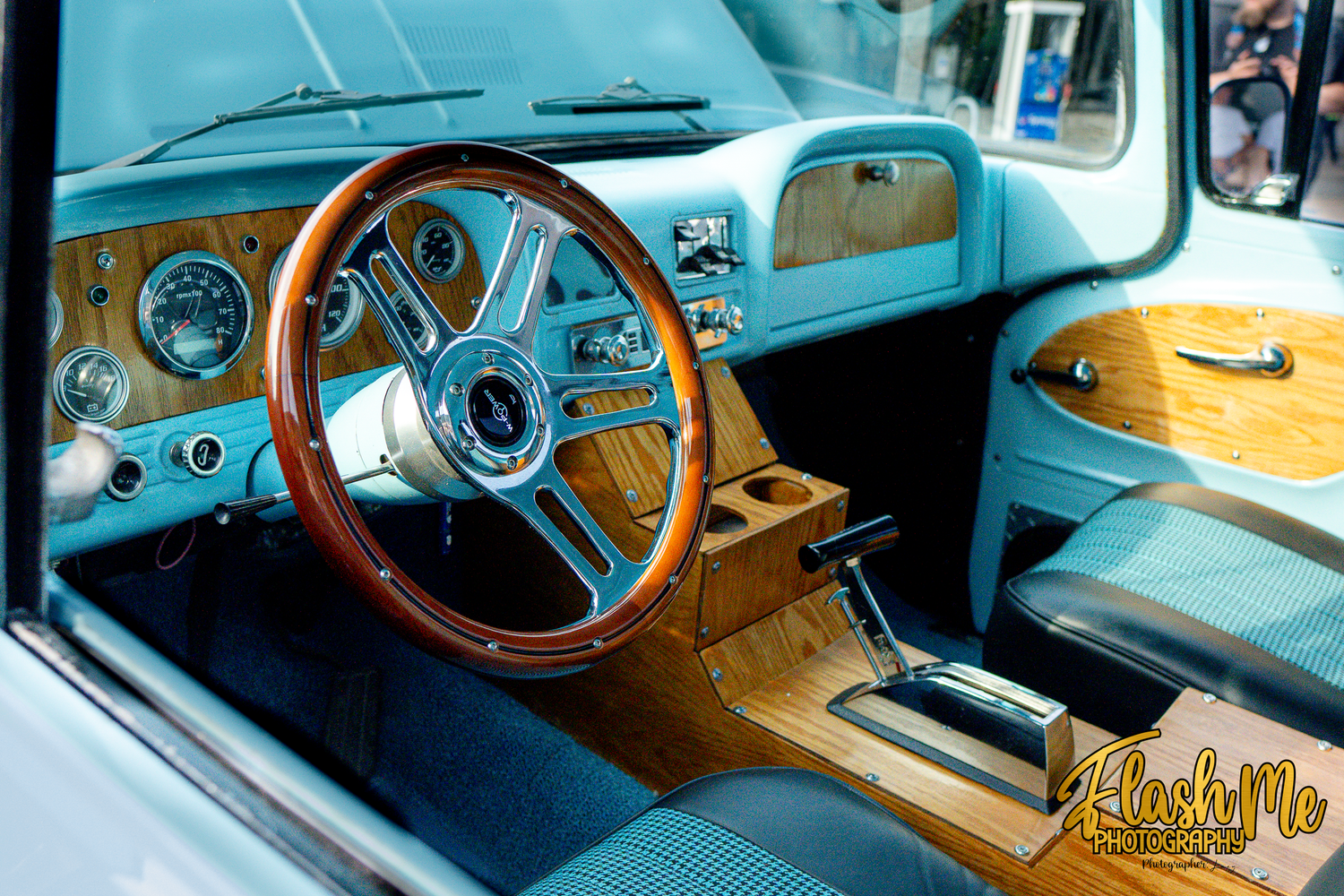 Vintage car interior with teal upholstery, wood grain dashboard, and classic wooden steering wheel.