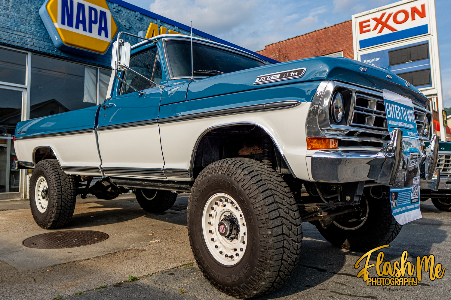 Vintage lifted blue Ford F-250 4x4 pickup truck parked near NAPA and Exxon storefronts.