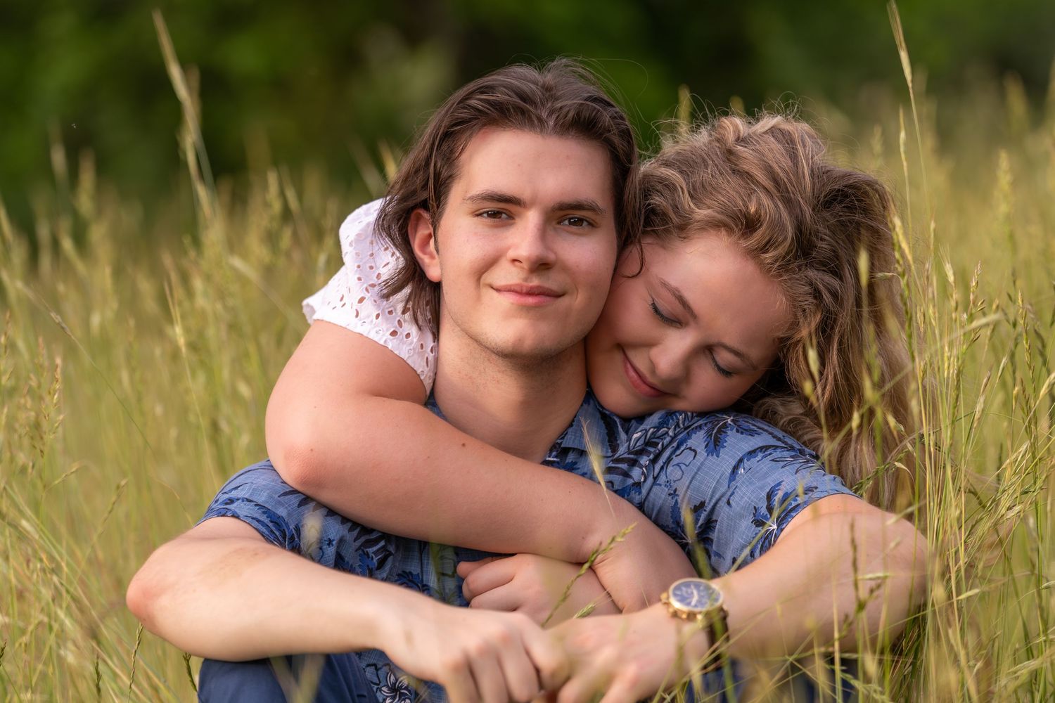 Young couple cuddling together in a tall grass field, sharing a tender moment.