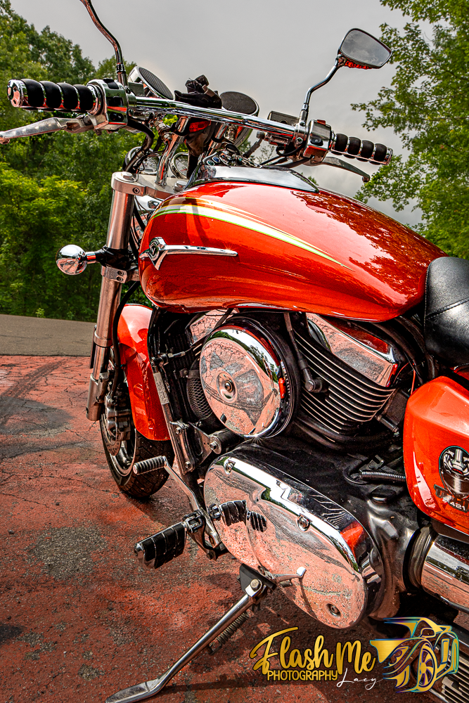 Shiny orange Kawasaki Vulcan cruiser motorcycle with chrome engine details parked outdoors.