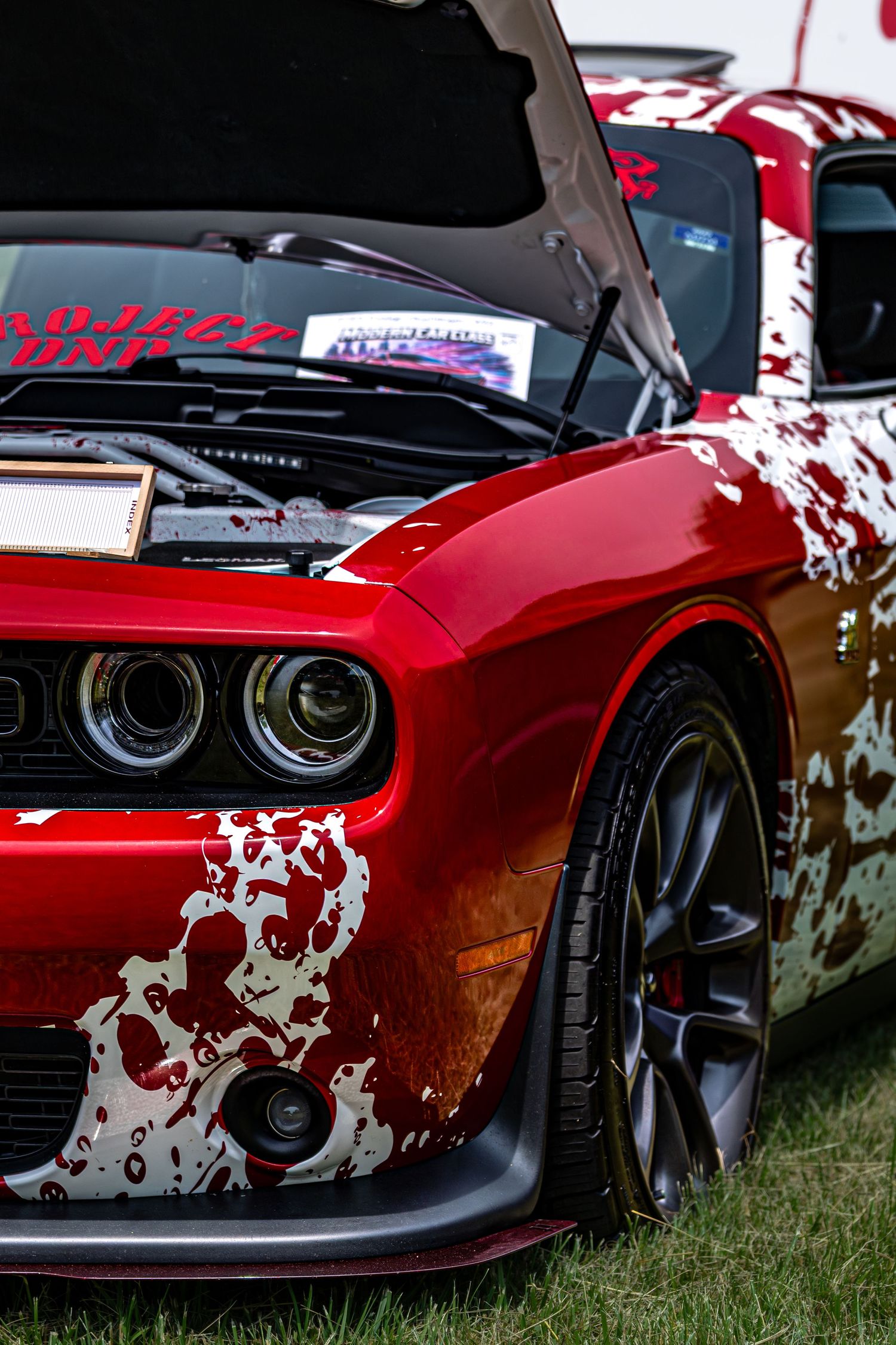 Red Dodge Challenger with skull wrap custom paint job and open hood at a car show.