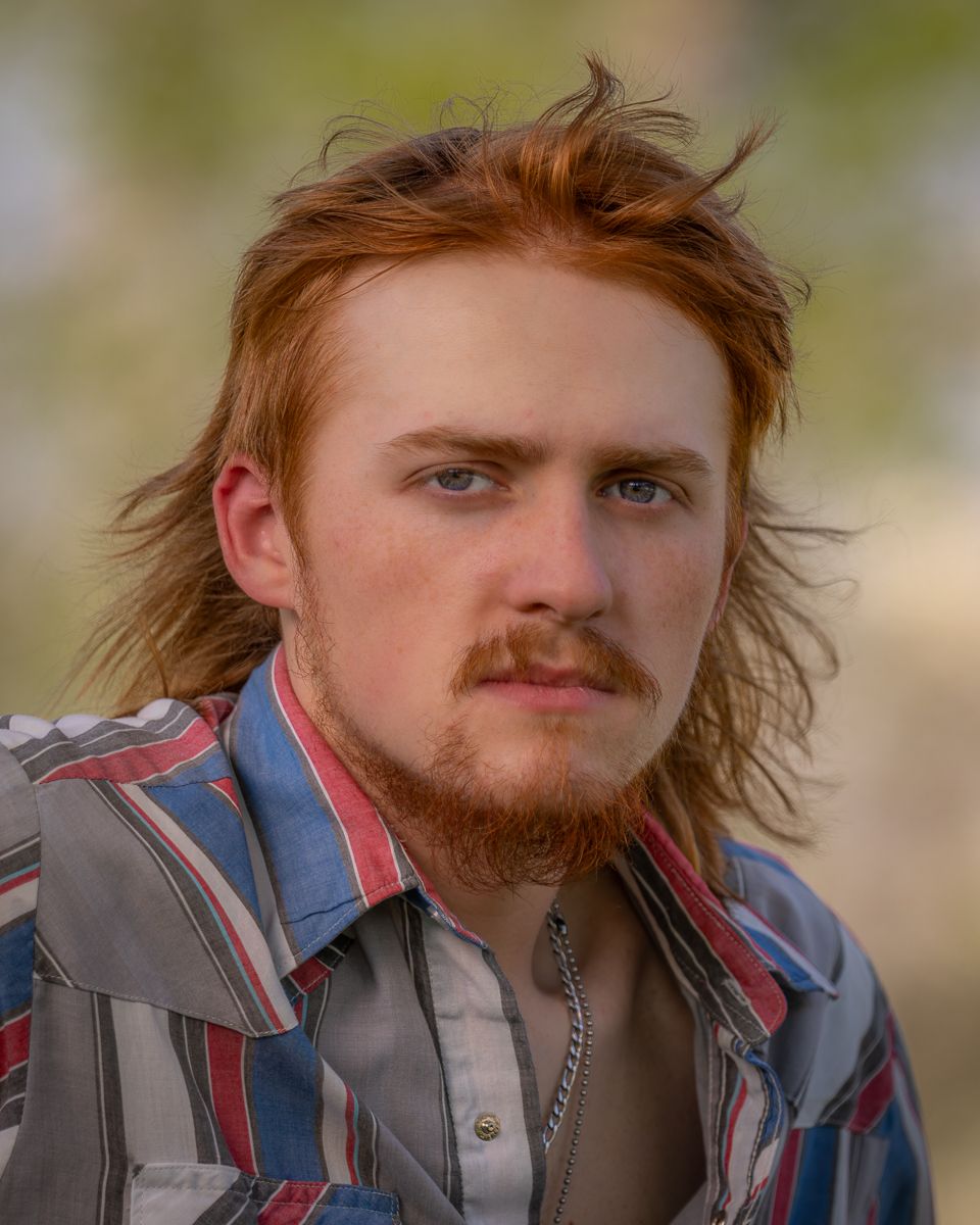 Portrait of a young man with red hair and beard wearing a plaid shirt with bokeh green background.