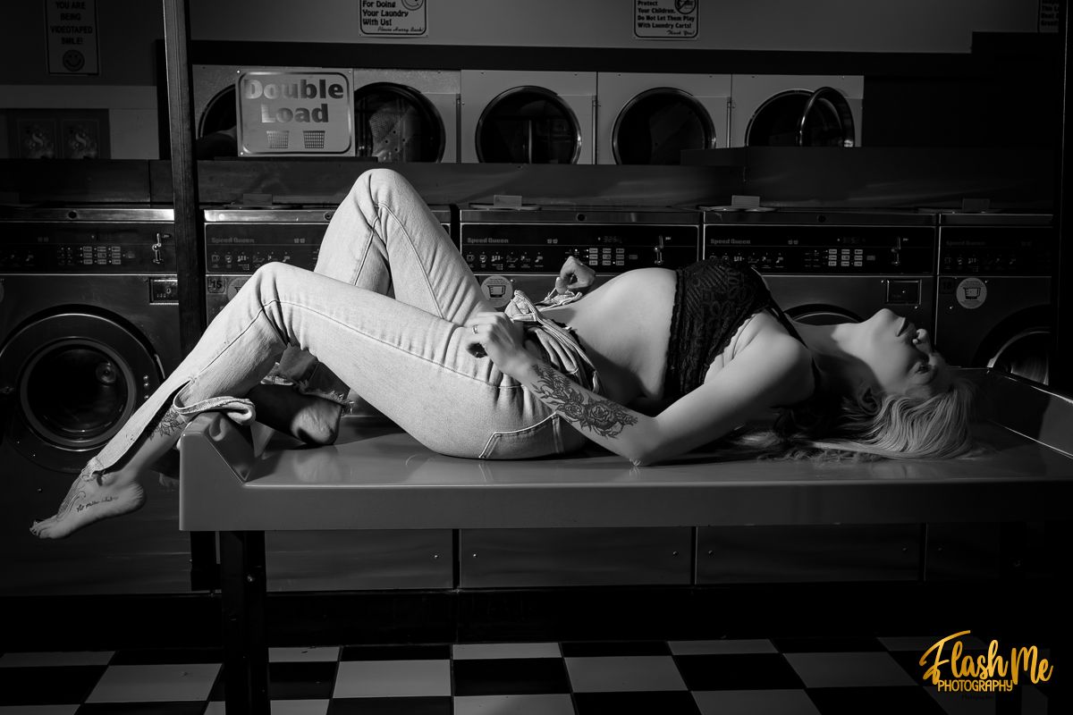 Black and white photo of a couple posing romantically on a folding table in a vintage laundromat.
