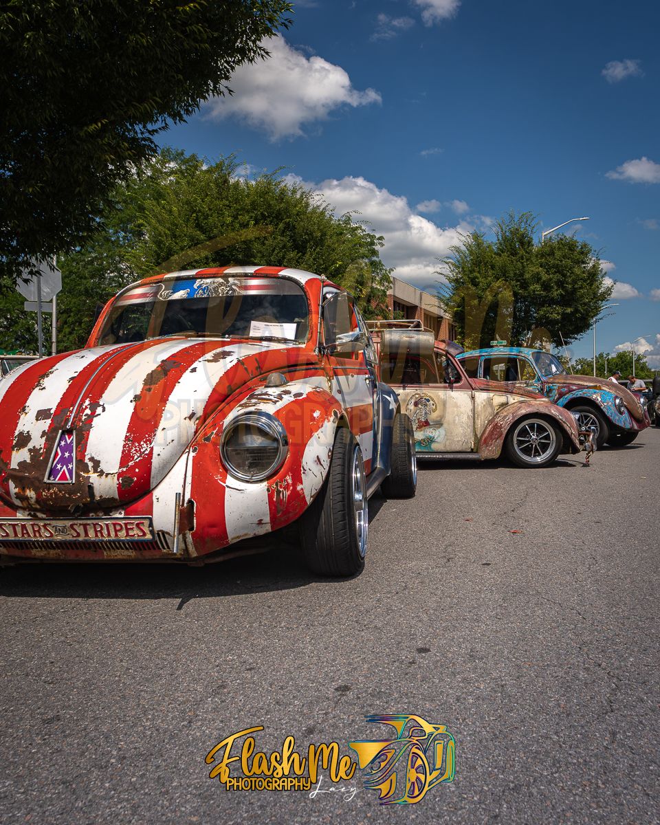 Vintage VW Beetles with Stars and Stripes paint job displayed at an outdoor classic car show.