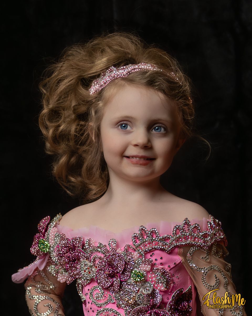 Young girl in sparkly pink pageant dress with rhinestone headband posing for portrait.