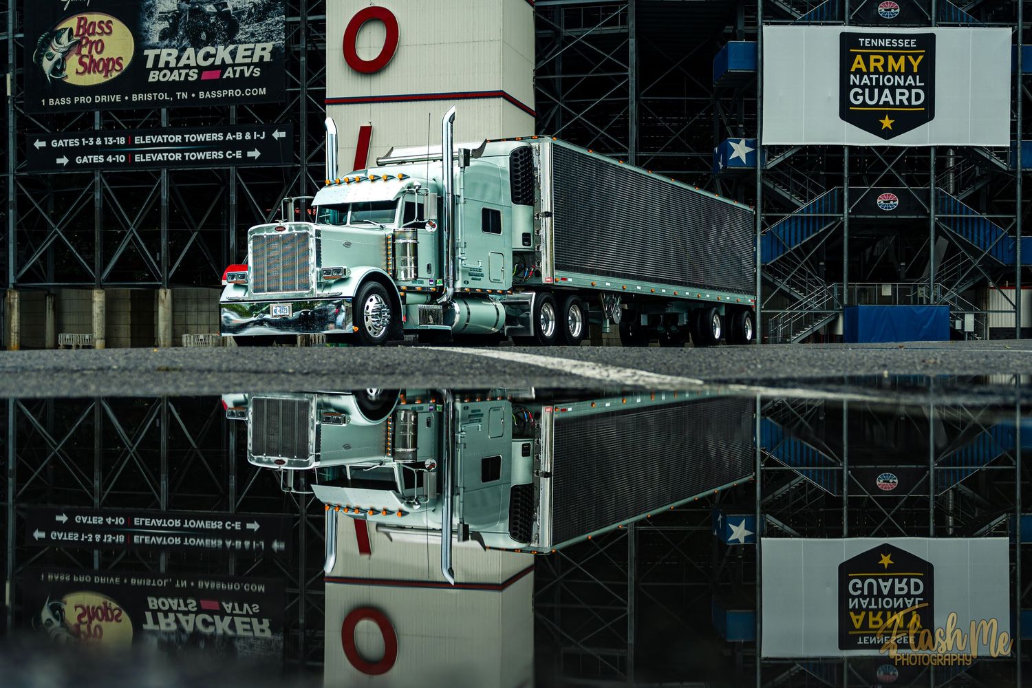 A white Peterbilt semi-truck reflects in a puddle outside a venue with Army National Guard signage.
