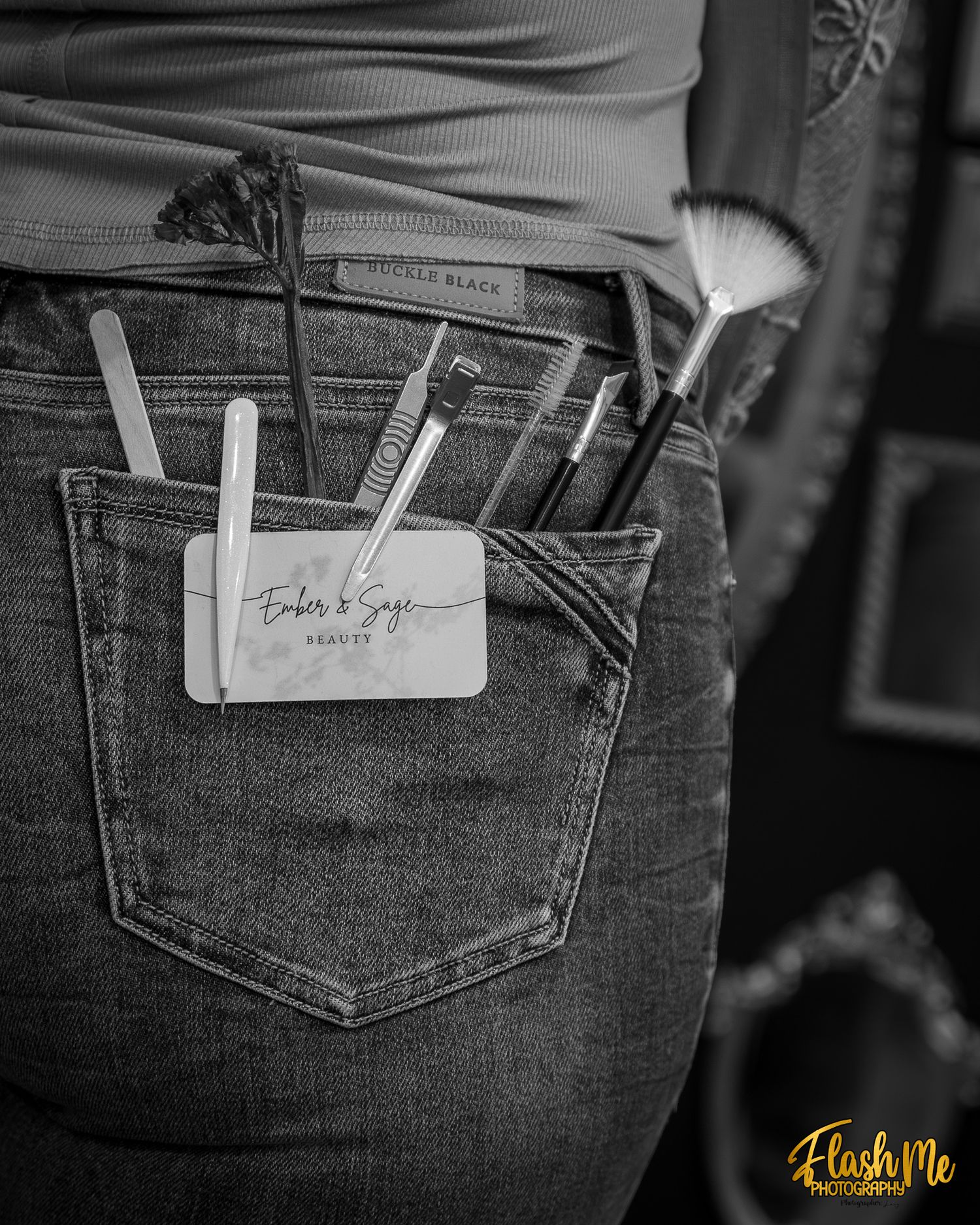 Black and white photo of beauty tools and business card tucked into the back pocket of denim jeans.