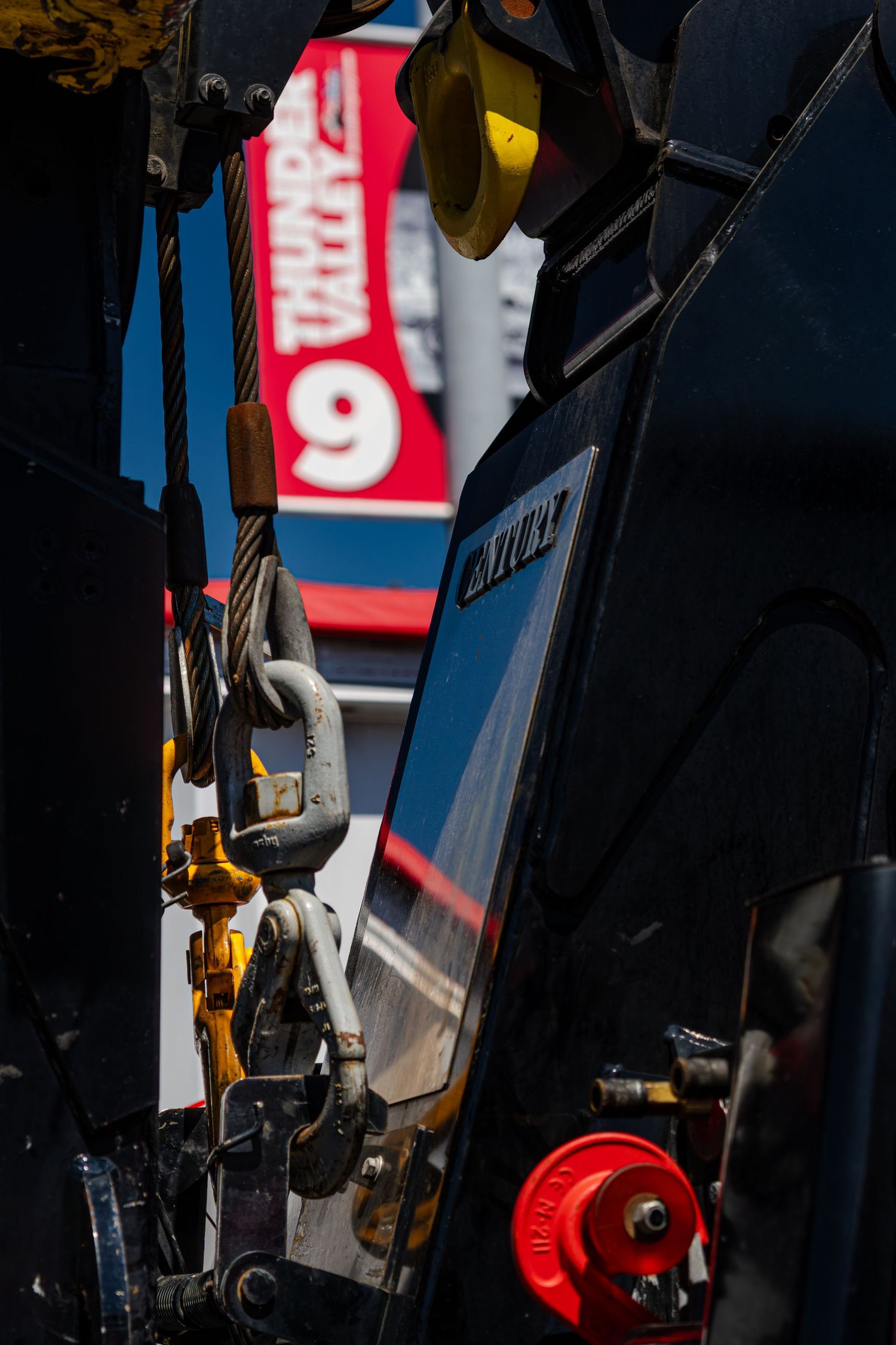 Close-up of heavy-duty tow truck hook and cable equipment with red racing signage behind.