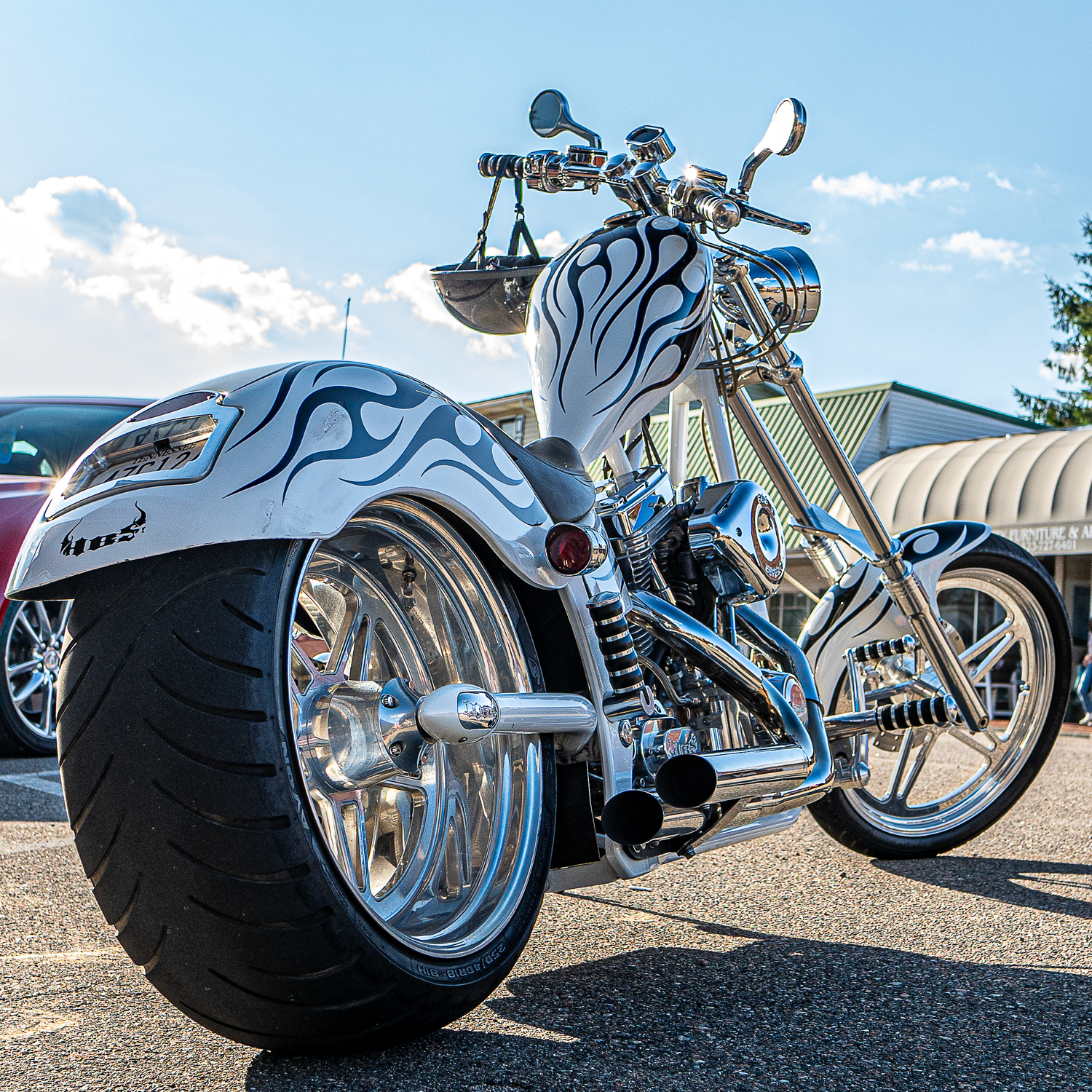 Custom chrome chopper motorcycle with flame graphics and oversized tires in a parking lot.