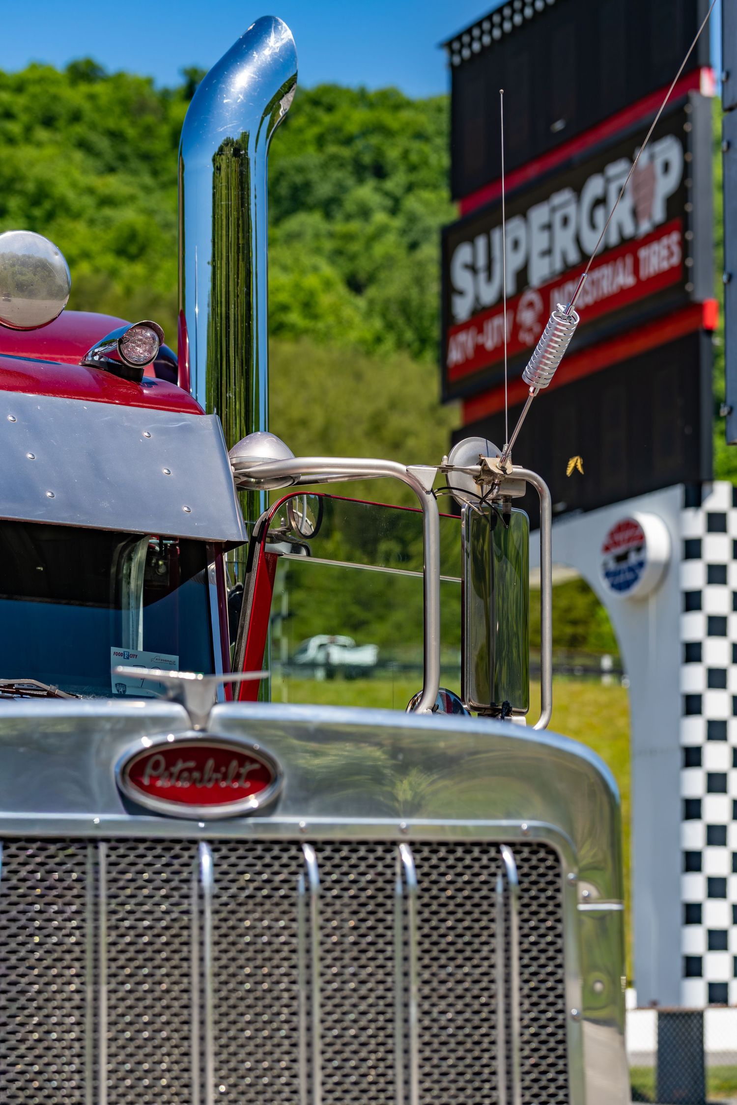 A shiny red Peterbilt semi-truck with chrome details parked near a Supergrip tires sign outdoors.