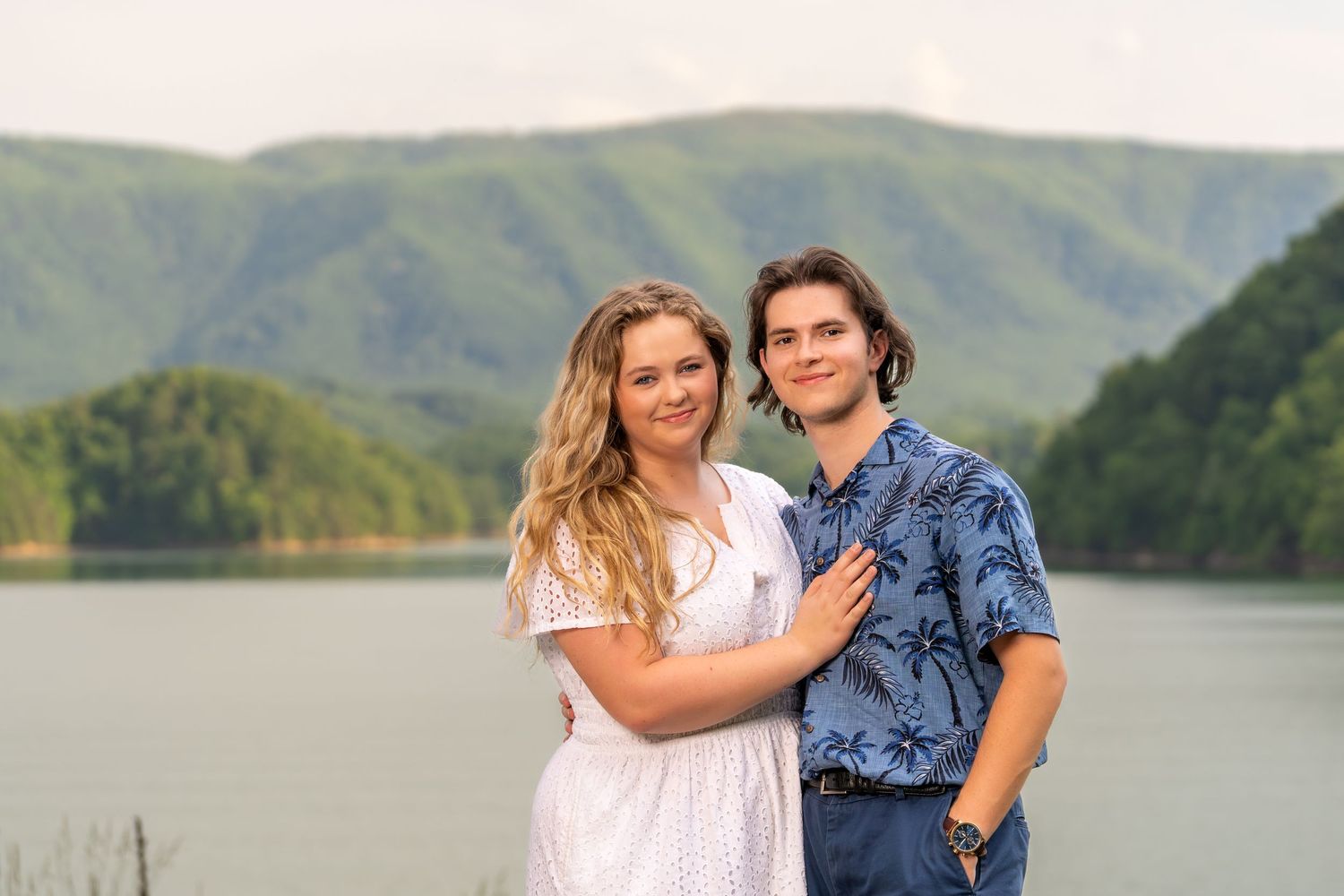 Young couple embracing and smiling together with a scenic mountain lake backdrop.