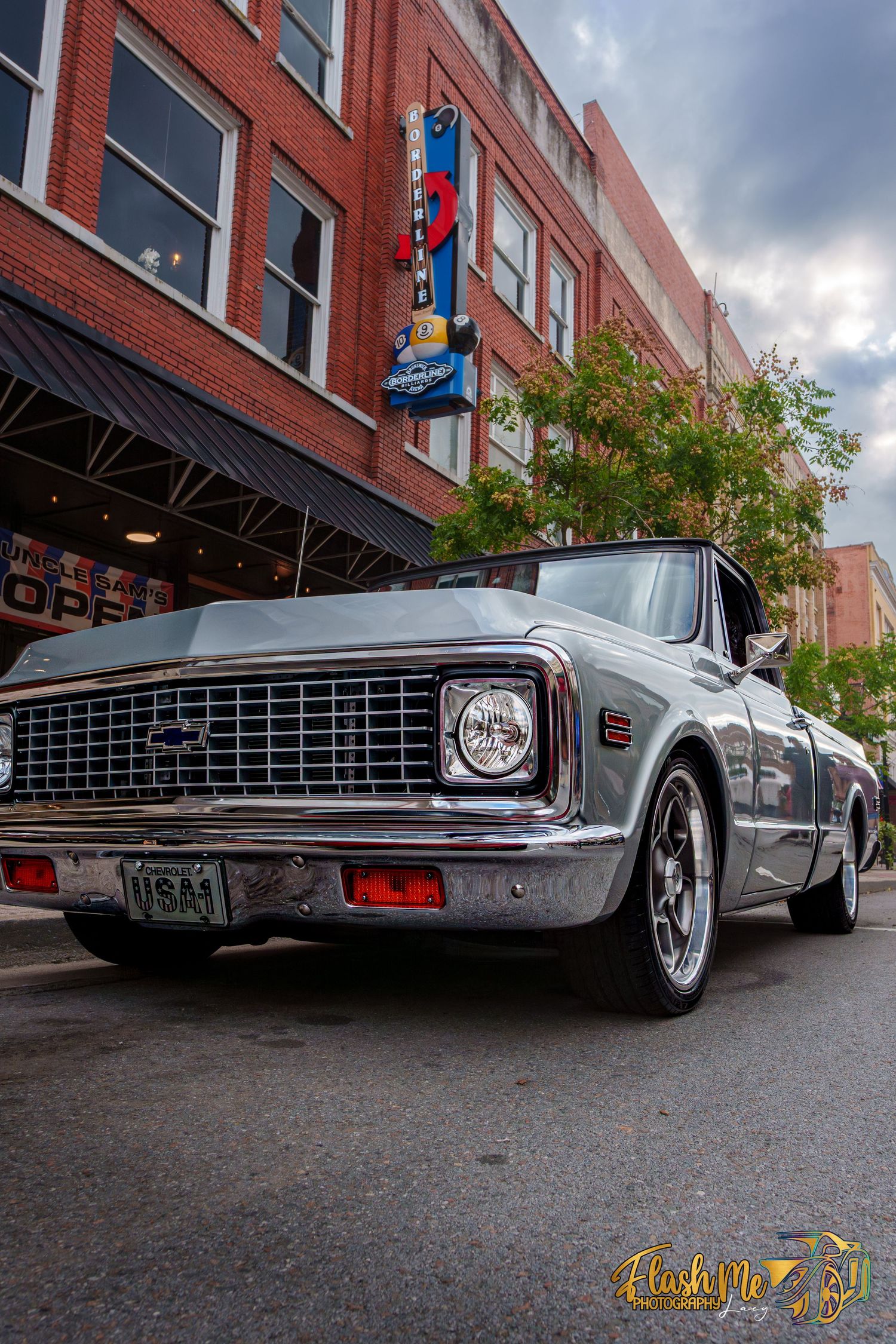 Silver classic Chevrolet C10 pickup truck parked on an urban street near brick buildings.