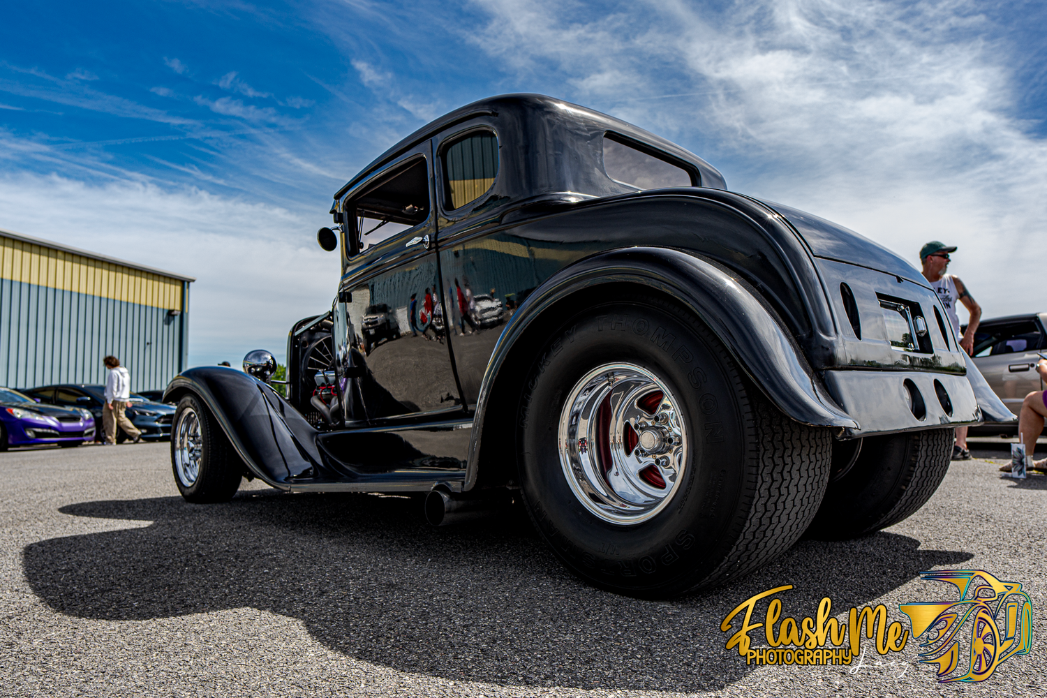 Sleek black vintage hot rod with large rear tires photographed from a low angle at an outdoor car show.