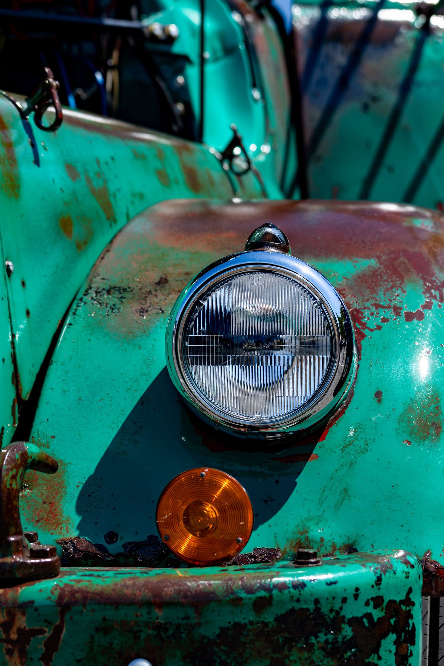 Close-up of a round chrome headlight on a rusty vintage turquoise truck with aged patina paint.