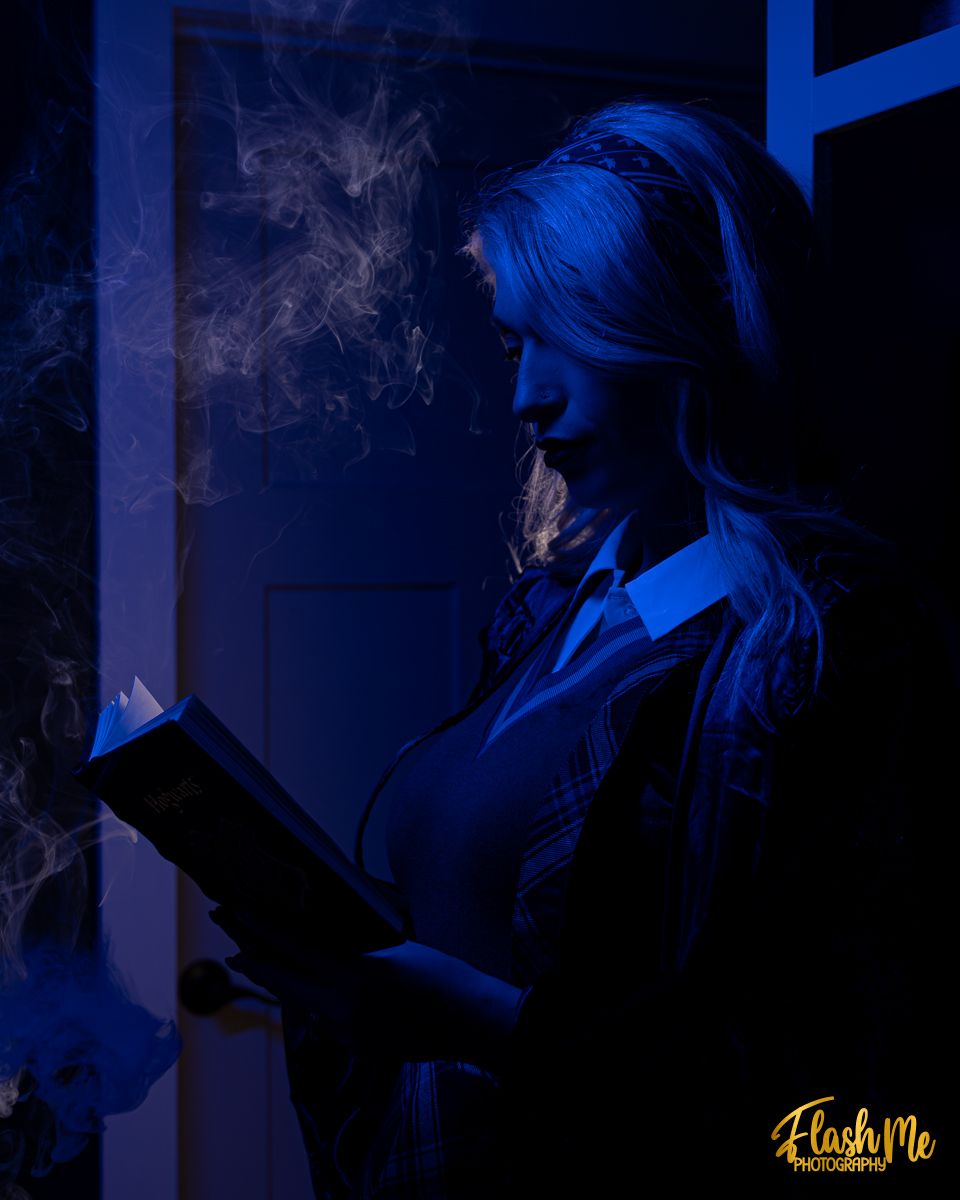 Dramatic blue-lit silhouette of a woman reading a glowing book with smoke swirling around her in darkness.