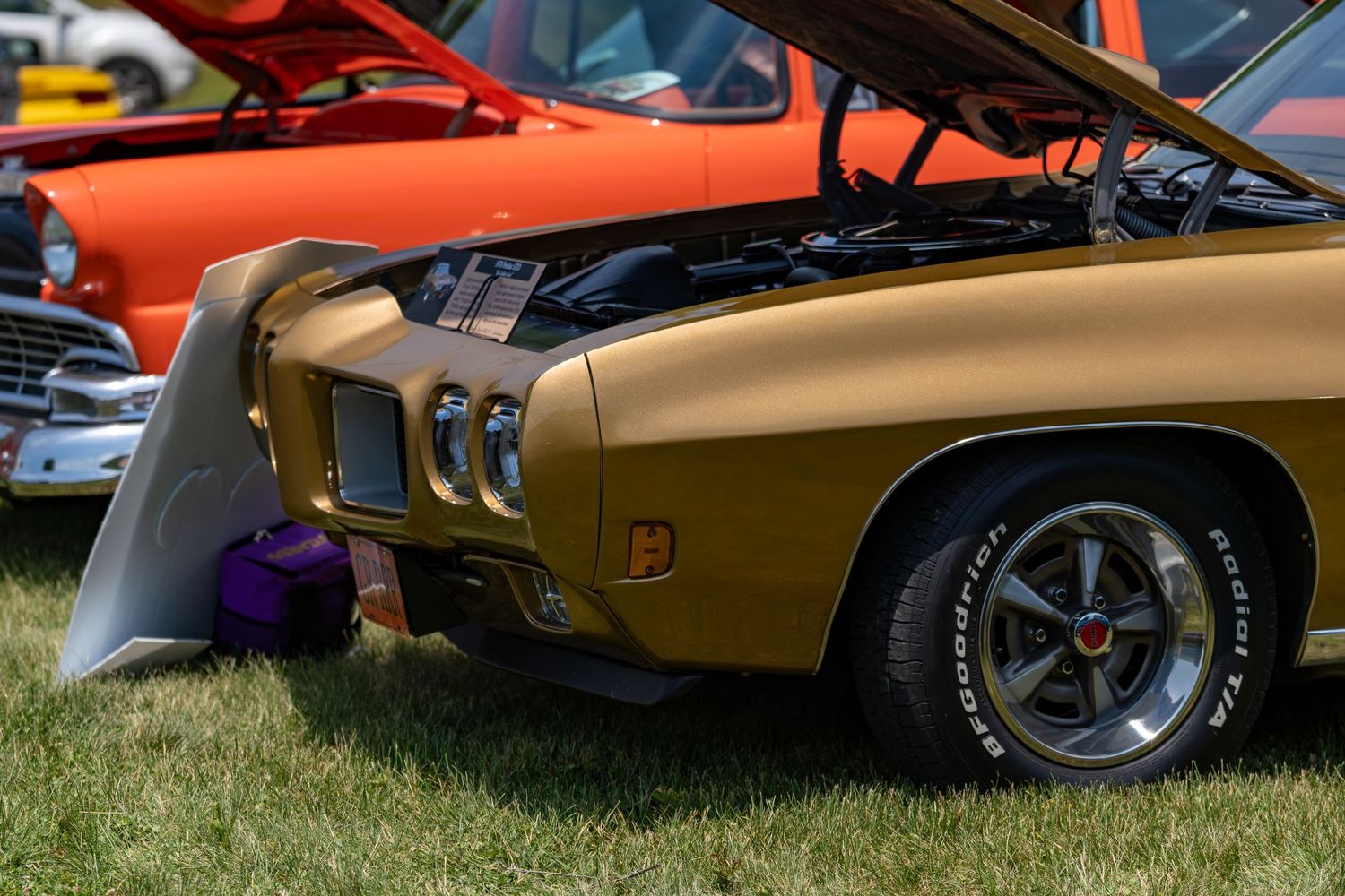 Gold classic Pontiac muscle car with open hood on display at an outdoor car show.