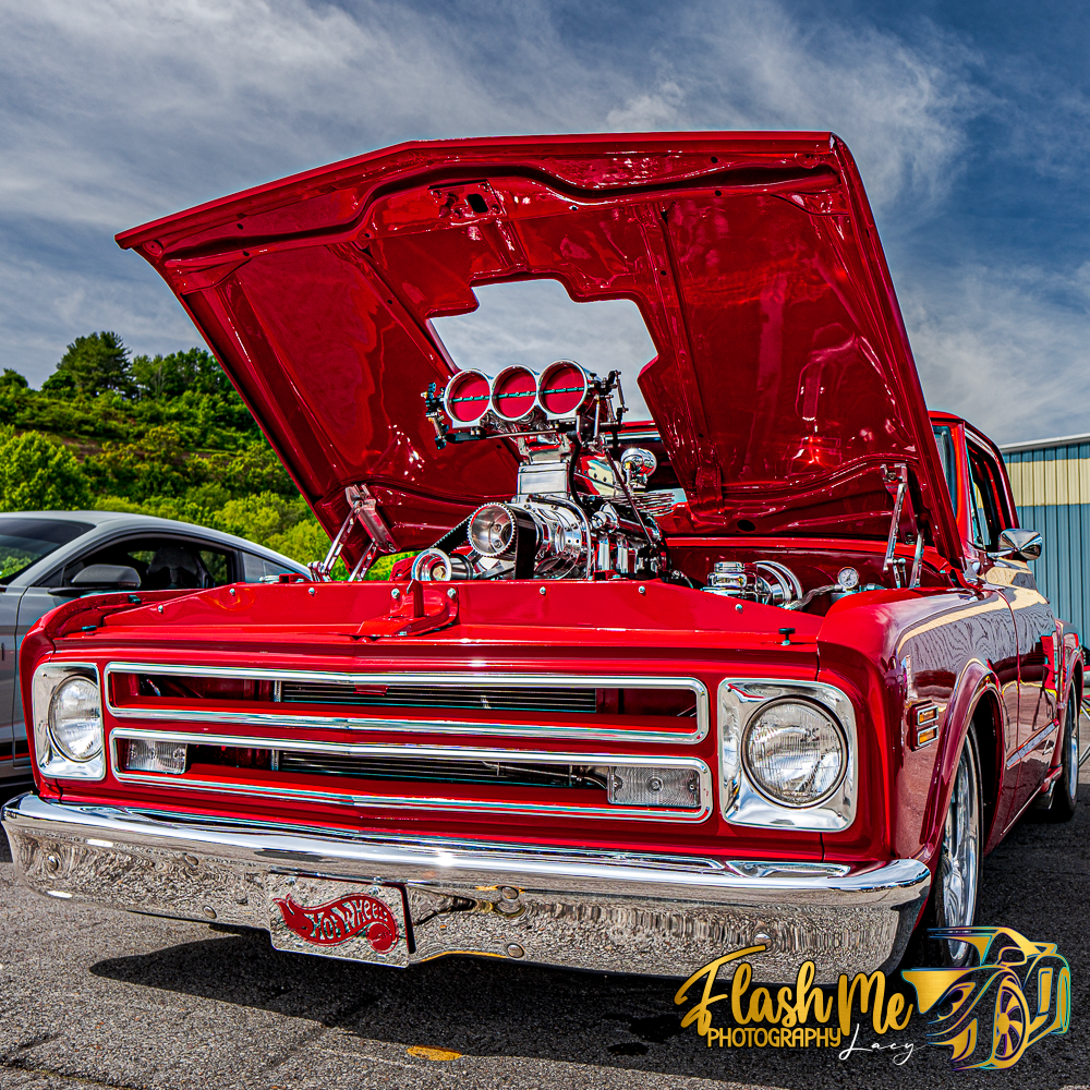 Classic red Chevy C10 truck with hood open revealing a supercharged engine at a car show.