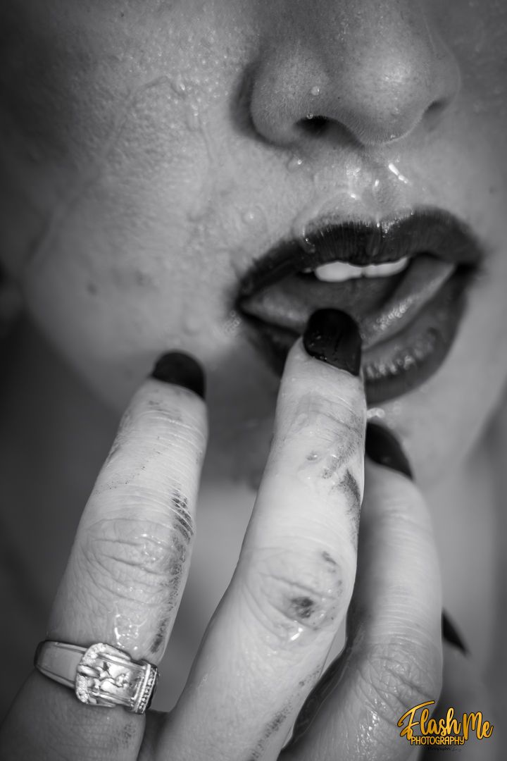 Black and white close-up of lips and hand with diamond ring touched by a finger.