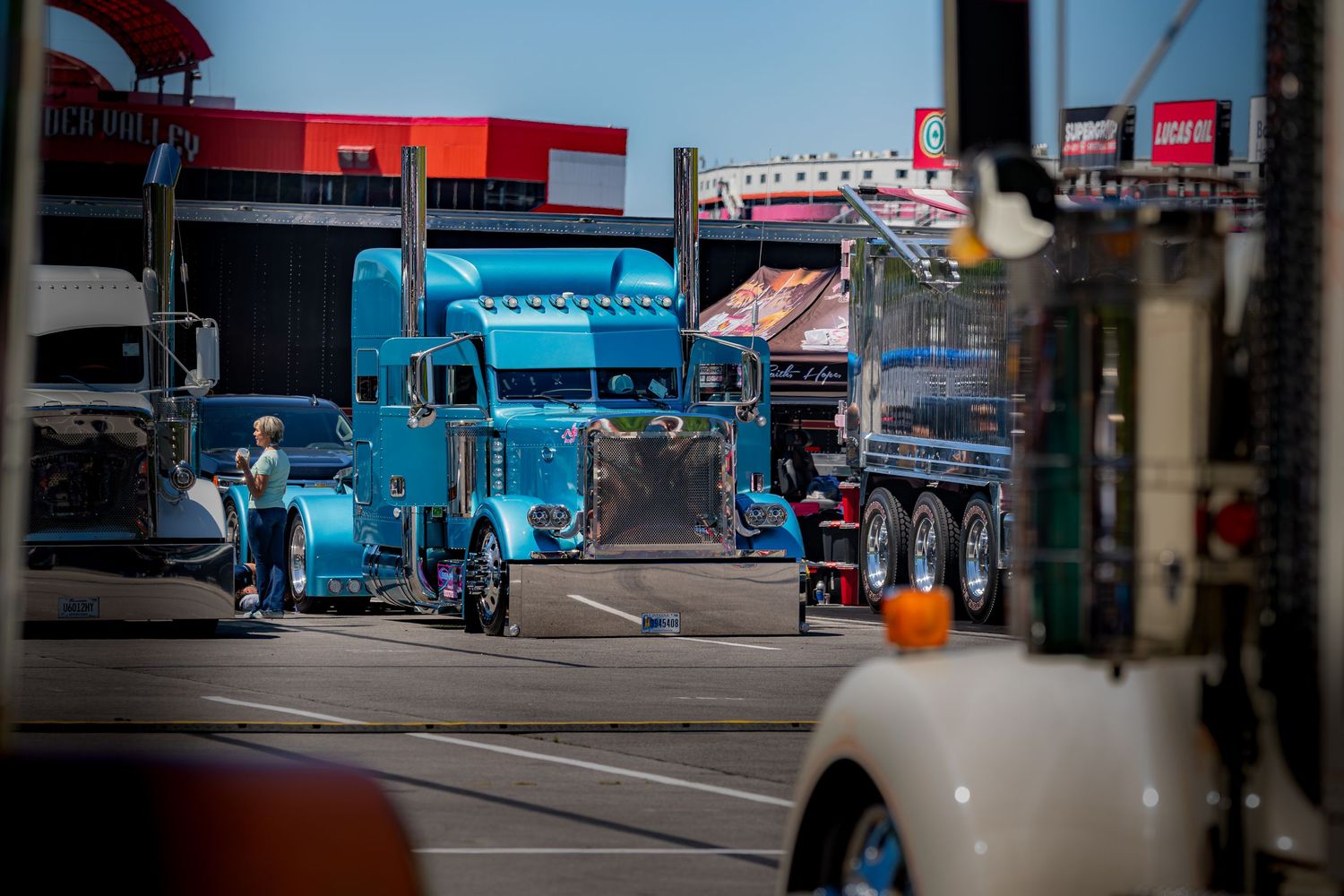 Blue custom semi-truck on display at outdoor trucking show on sunny day.