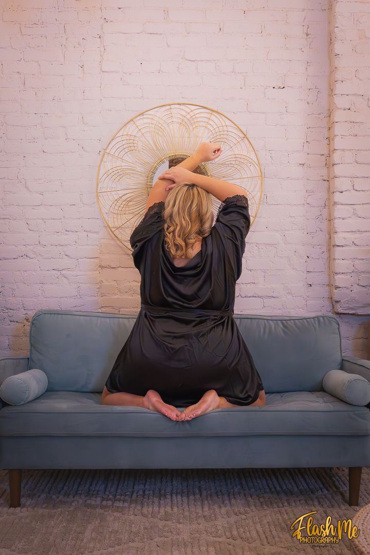 Woman in a dark robe sits on a blue sofa facing a decorative gold mandala on a white brick wall.