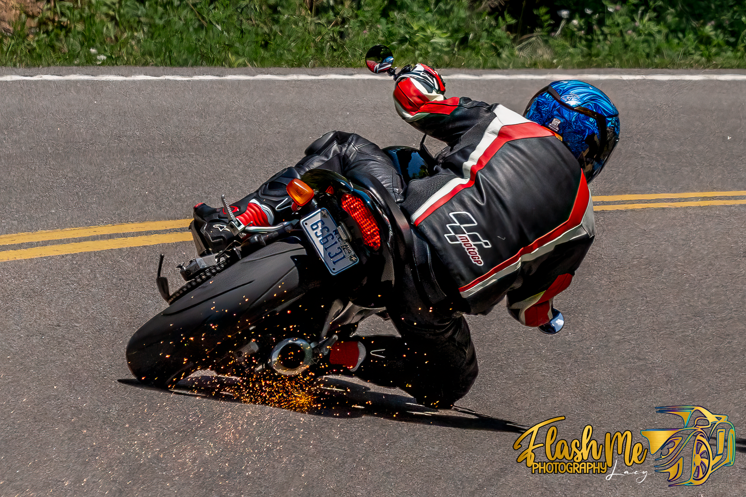Motorcycle racer leaning into a sharp turn with sparks flying from the footpeg on a winding road.