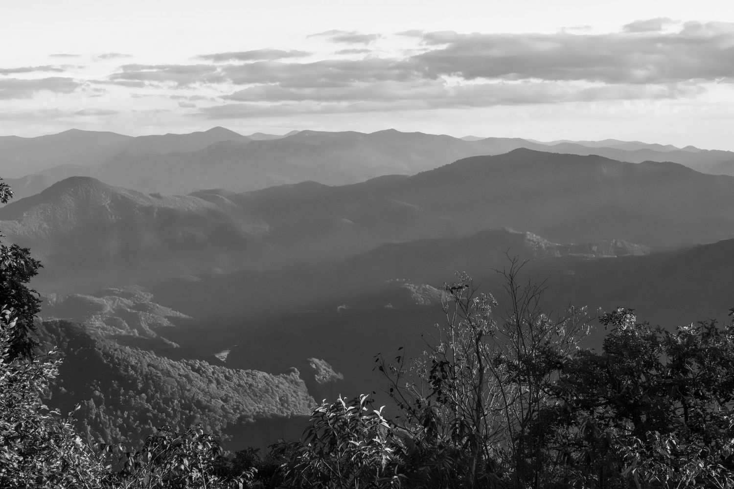 Black and white landscape photo of layered mountain ranges with misty valleys and dramatic clouds.