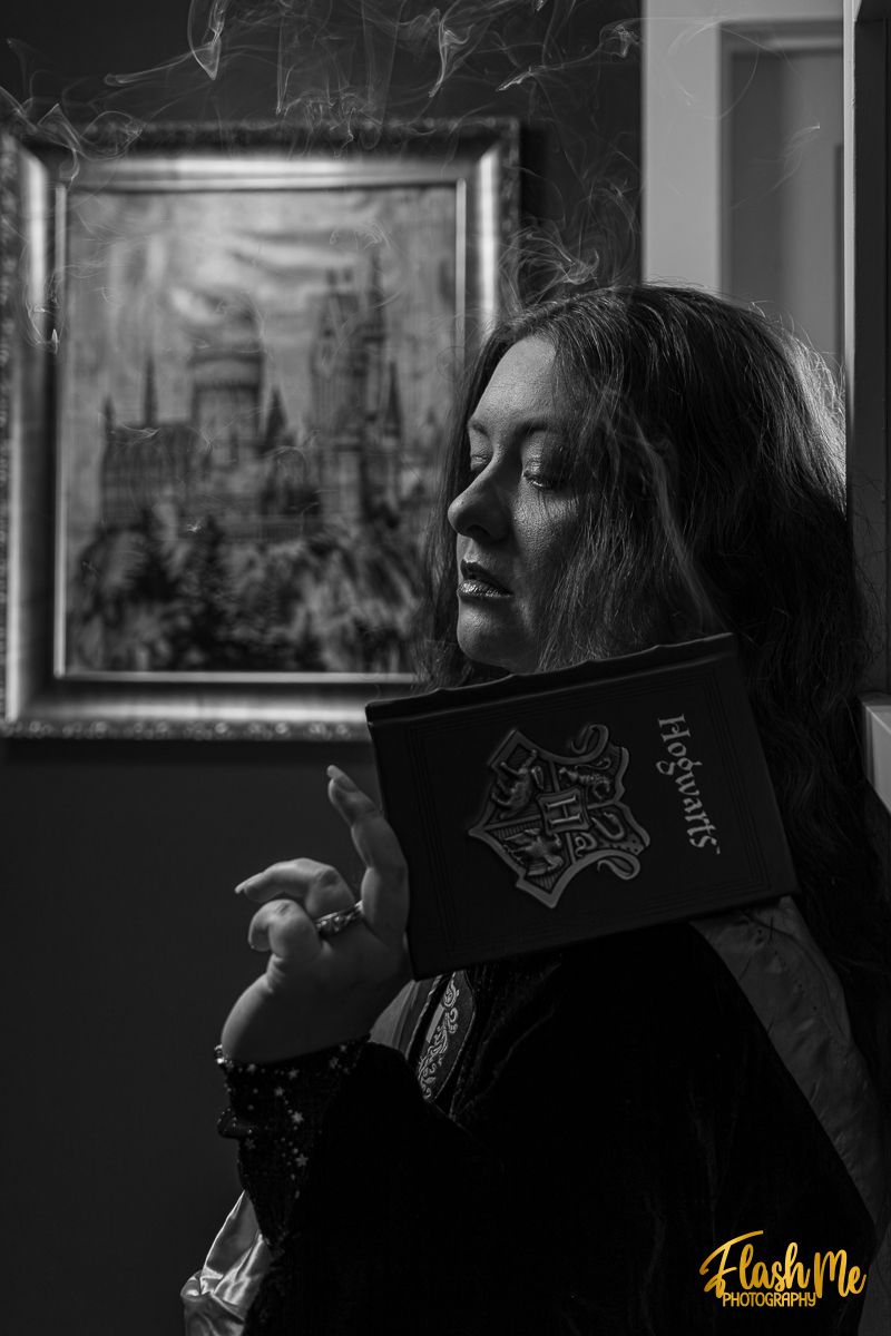 Black and white portrait of a woman holding a Hogwarts book with a castle painting in the background.