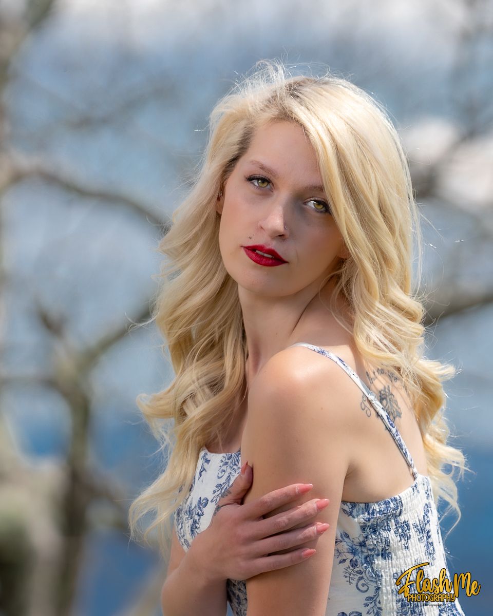 Blonde woman with red lips in floral dress posing outdoors with soft bokeh background.