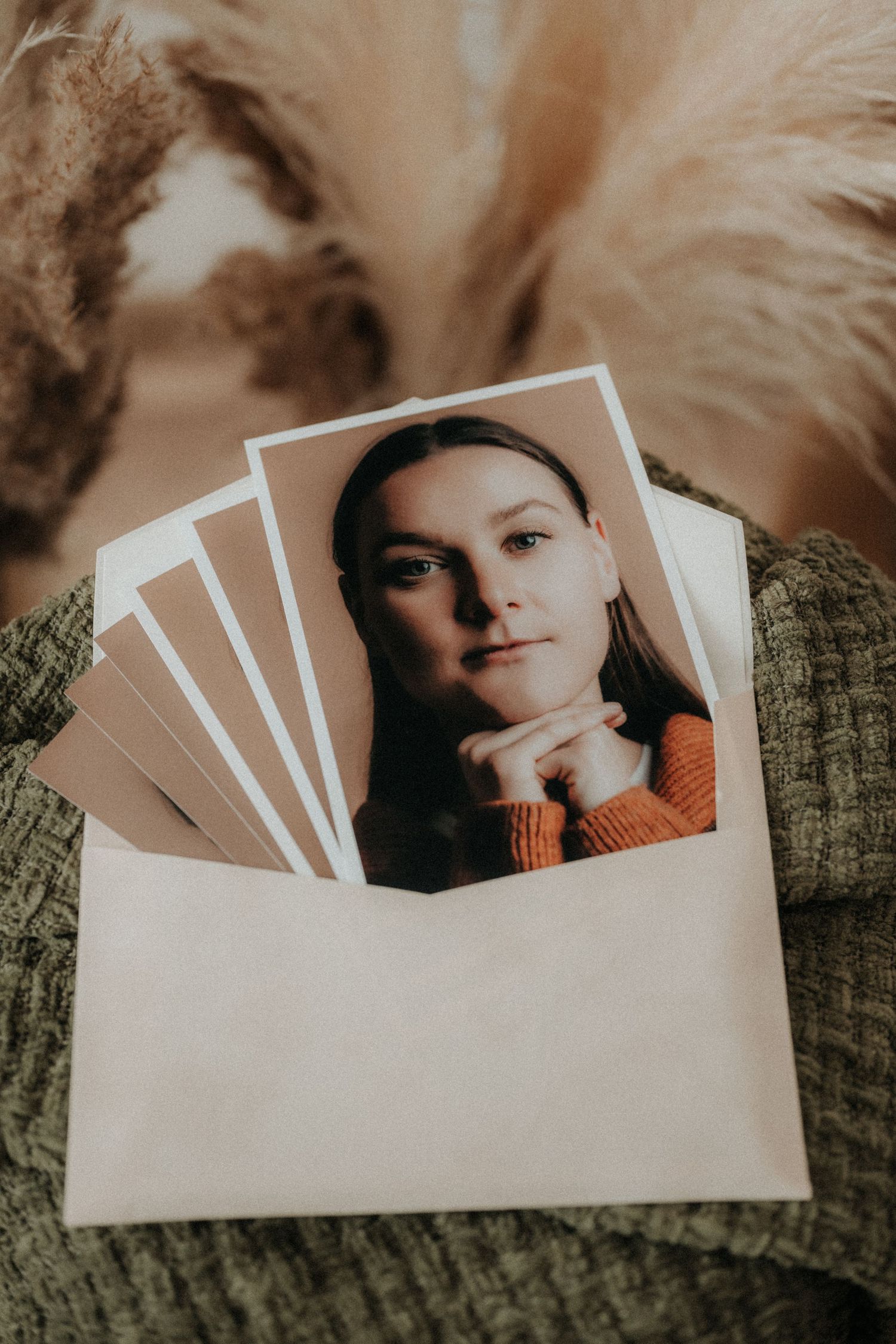 Woman in orange sweater posing in printed photo portrait inside an envelope, surrounded by dried pampas grass.