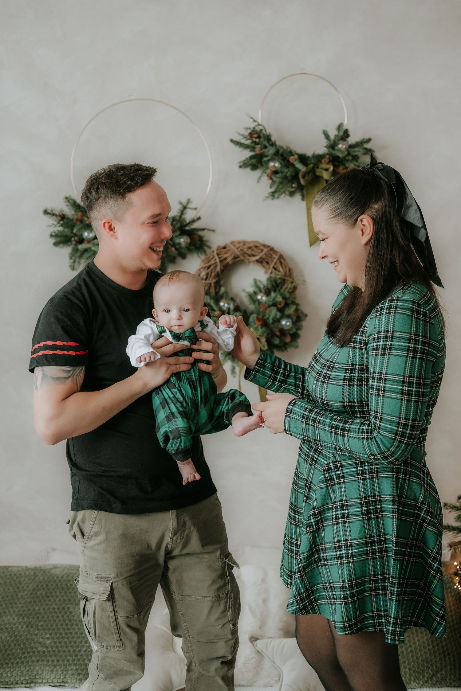 Happy family in festive outfits holding baby near Christmas wreaths holiday decor.