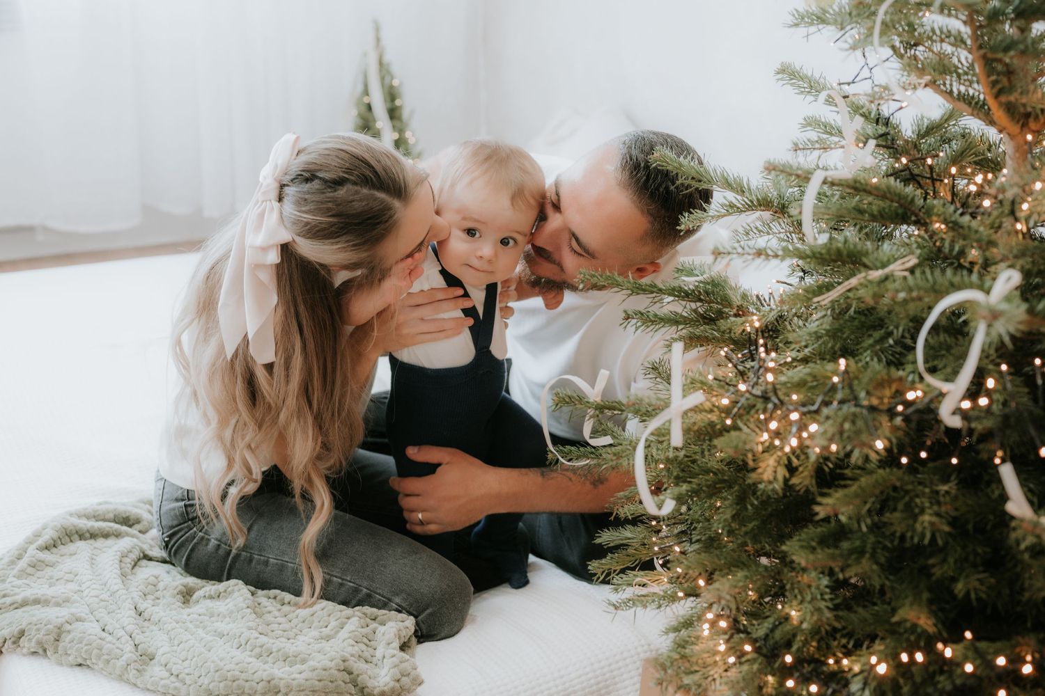 Family with baby celebrating Christmas by decorated tree with lights, sharing a joyful moment together.