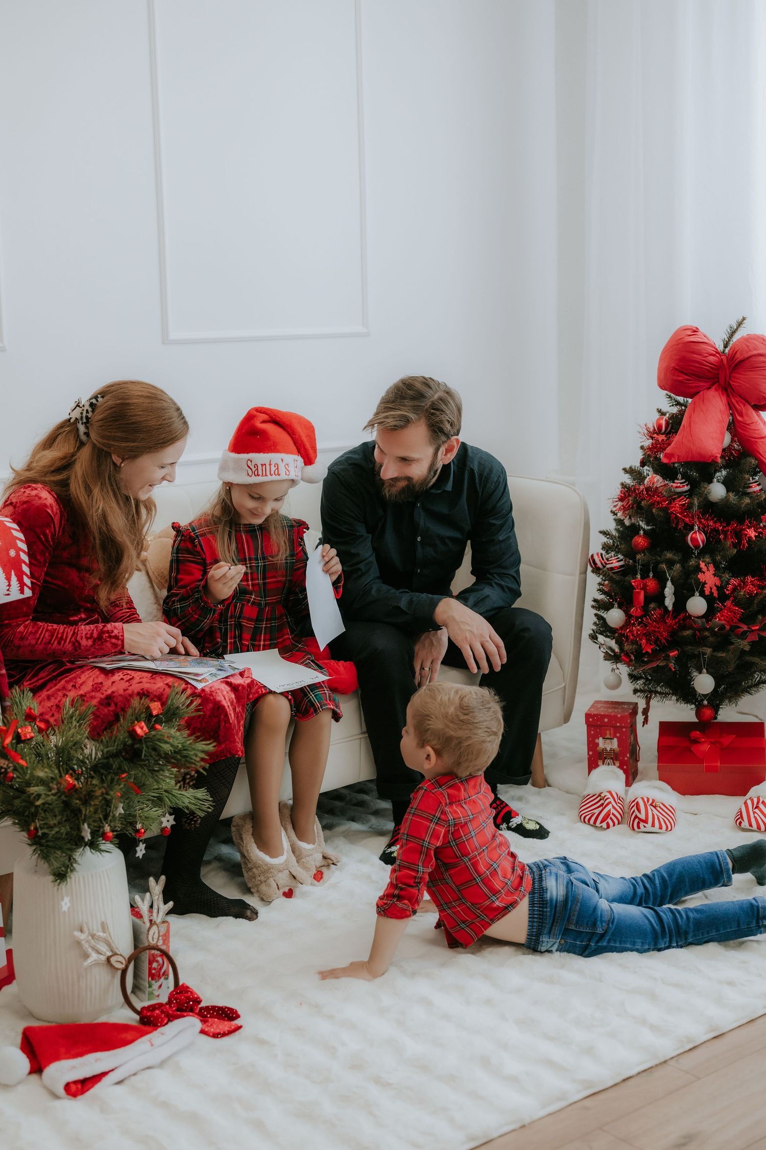 Family celebrating Christmas together, reading a letter to Santa near a decorated red and green Christmas tree.