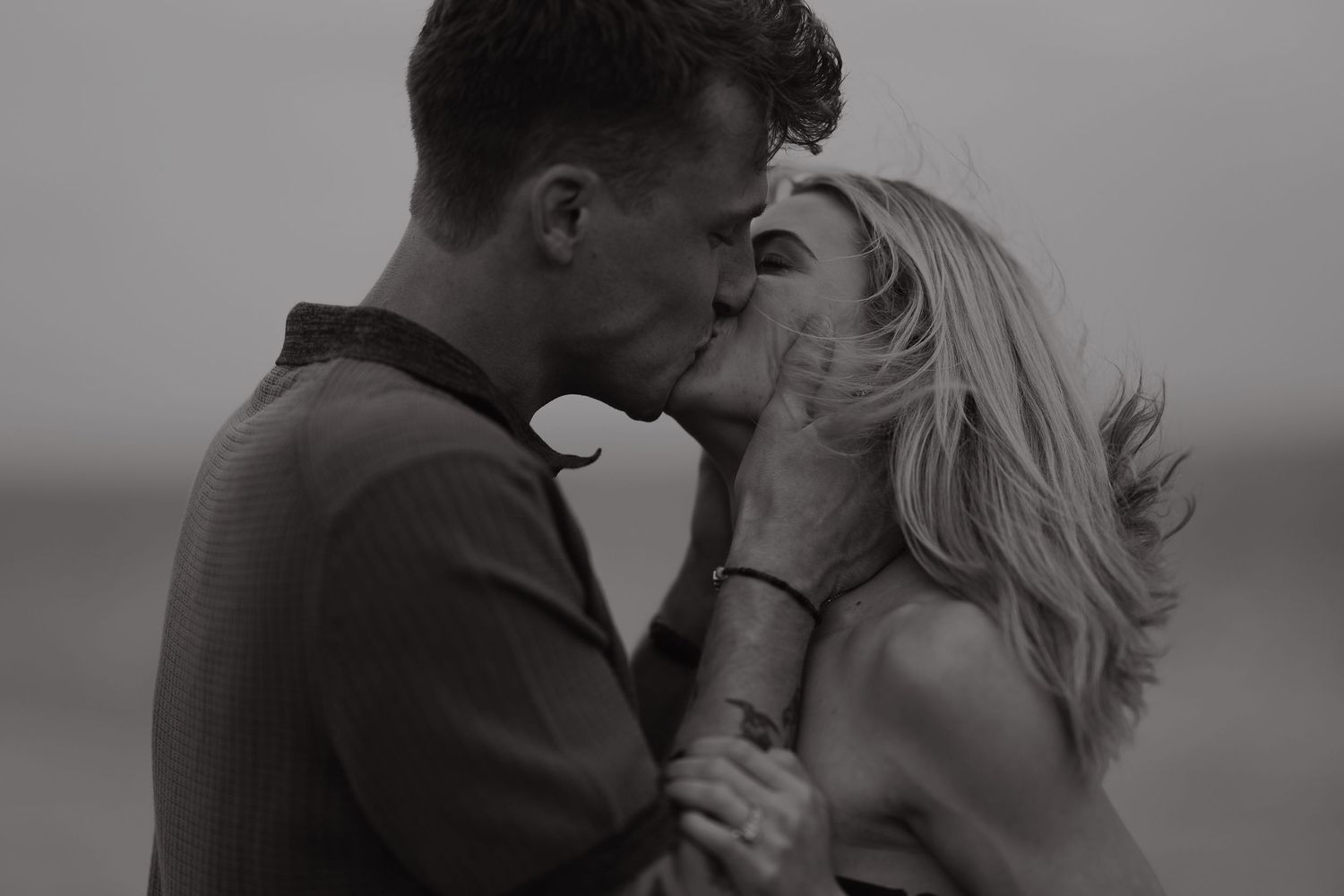 Black and white romantic photo of a couple sharing a tender kiss outdoors in the wind.