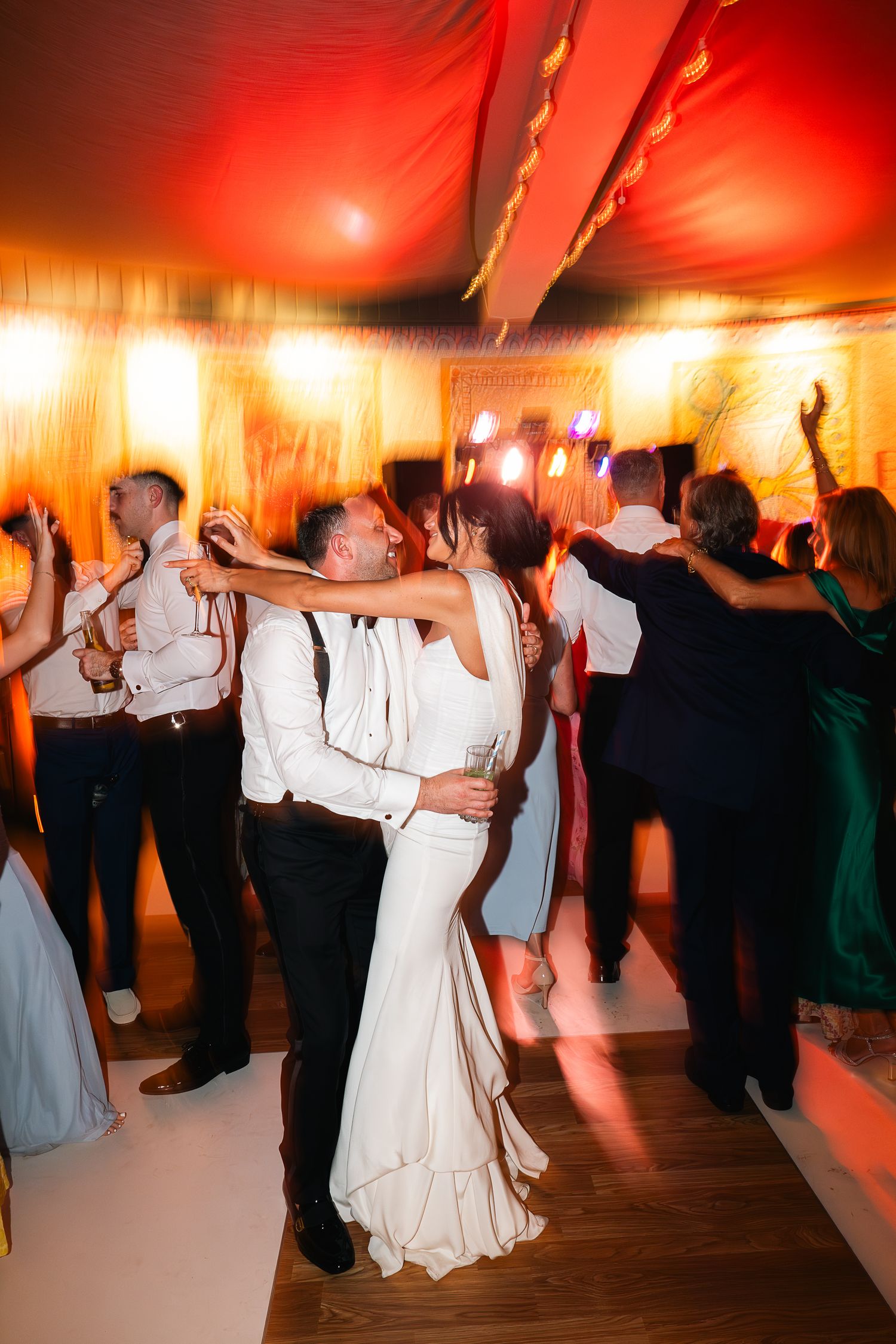 Bride and groom share a romantic first dance at their wedding reception under warm red and orange lighting.