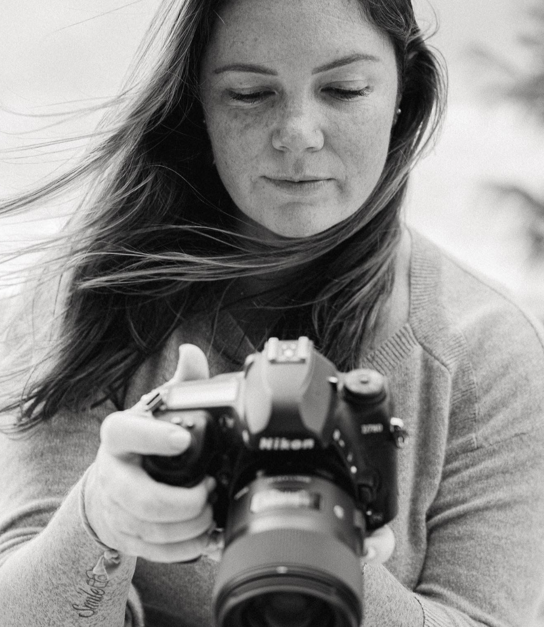 Close-up black and white portrait of a freckled woman reviewing images on a Nikon DSLR camera.