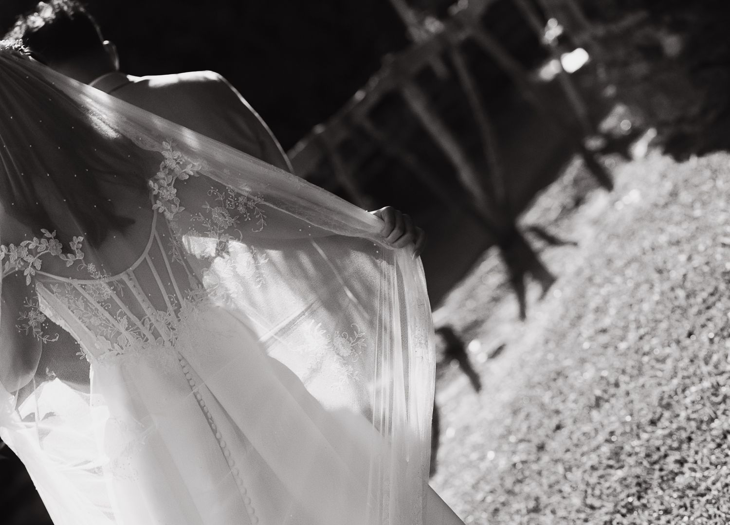 Black and white photo of a flowing bridal gown with lace veil billowing gracefully in the breeze outdoors.