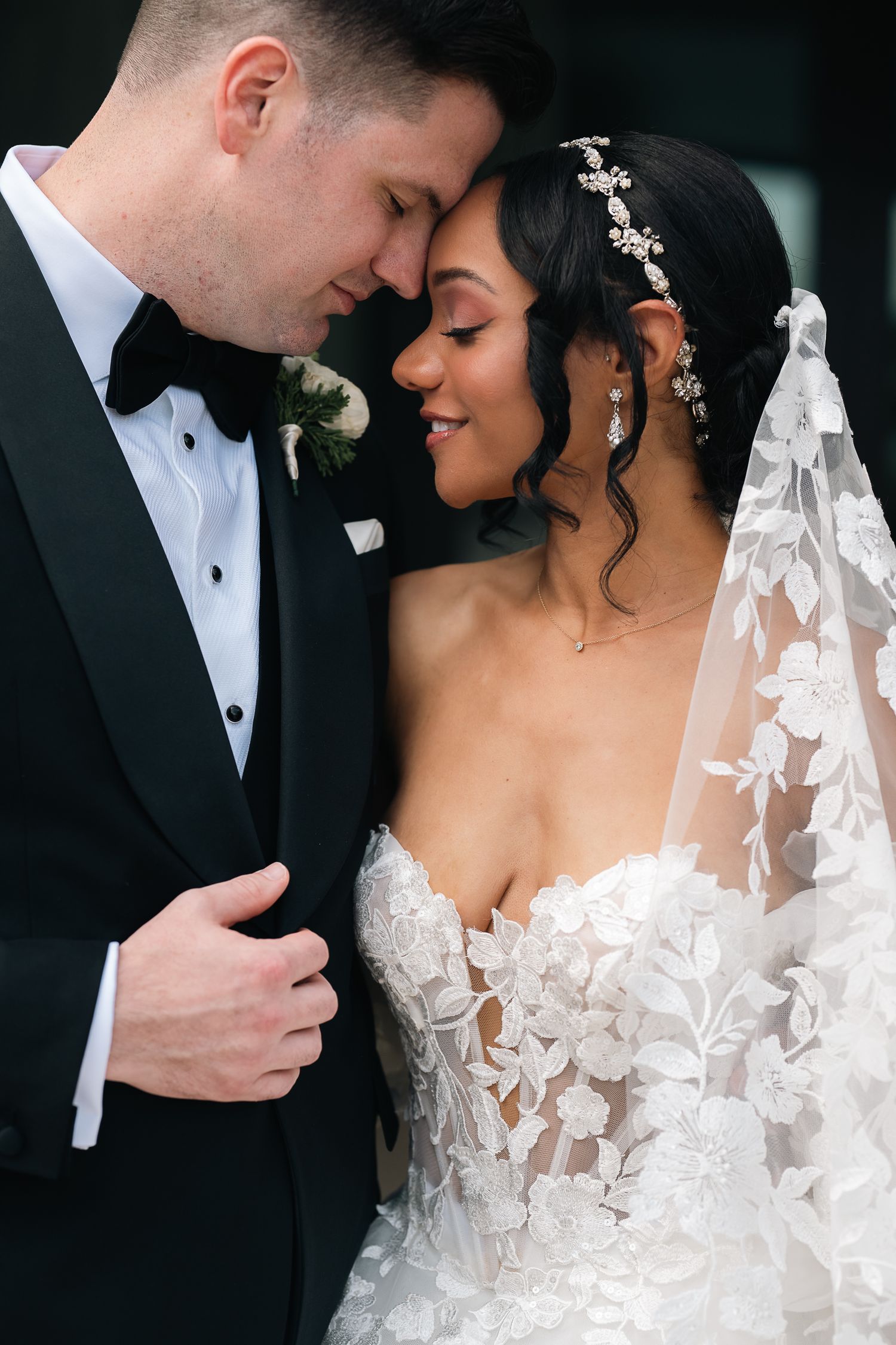 Bride and groom share an intimate forehead touch, bride in strapless lace gown with floral veil.
