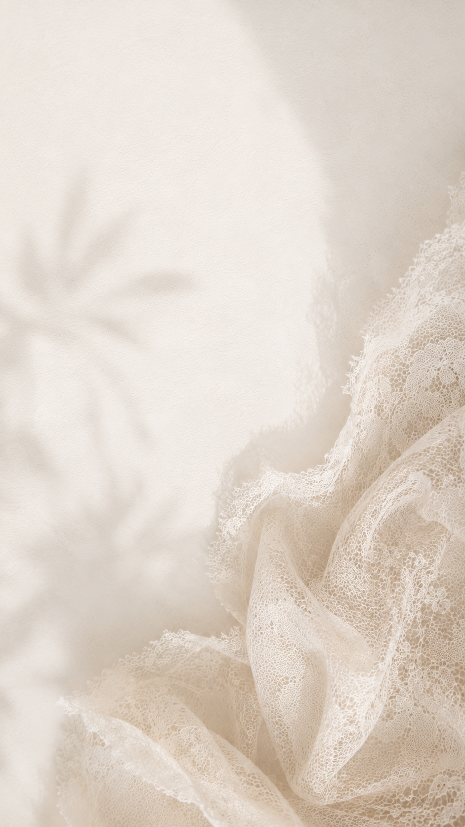 Luxurious white bridal lace fabric with soft leaf shadow overlay on a warm beige background.