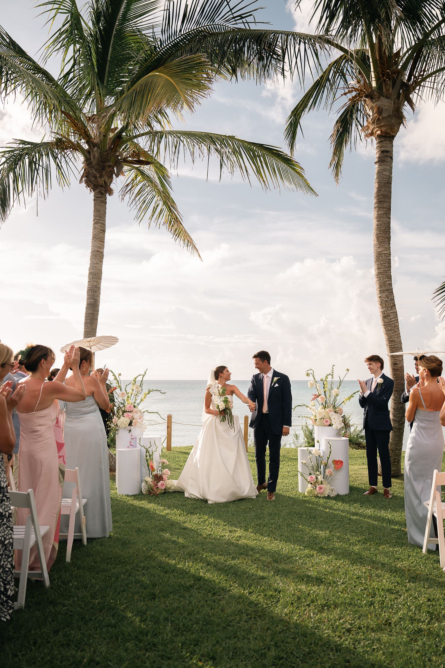 Newlyweds walking down the aisle at a tropical outdoor wedding ceremony by the ocean.