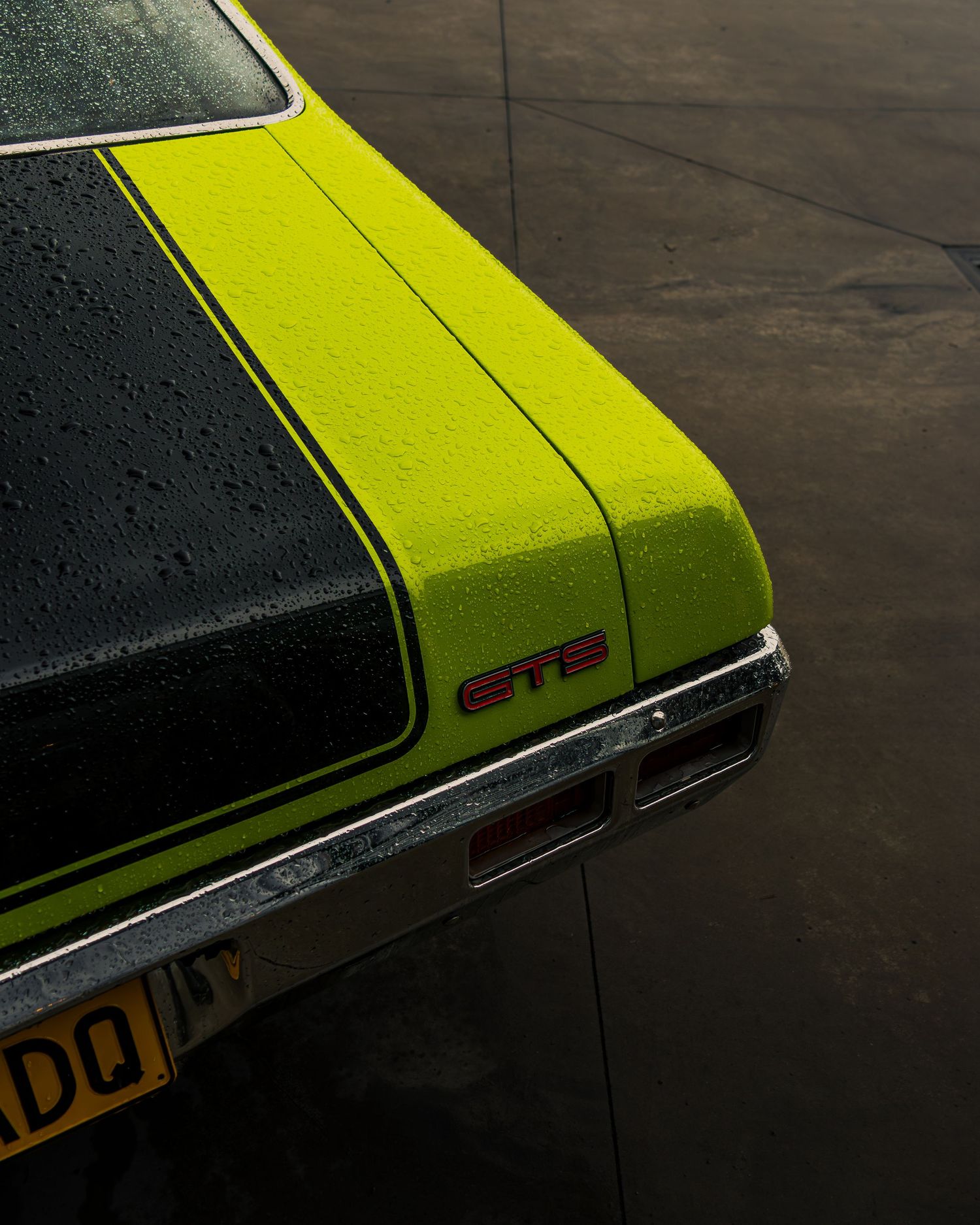 Rear quarter and badge detail of a yellow classic muscle car with black stripe