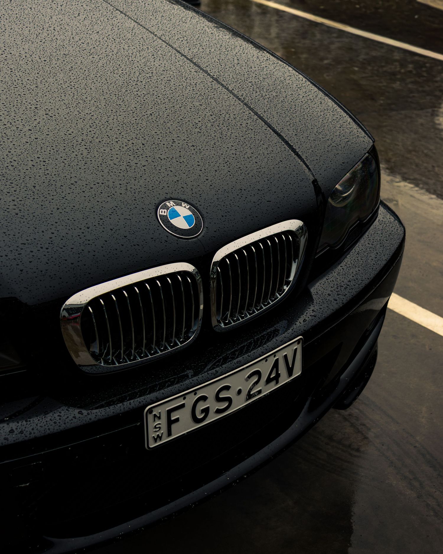 Front end and kidney grille of a dark BMW sedan photographed in the rain