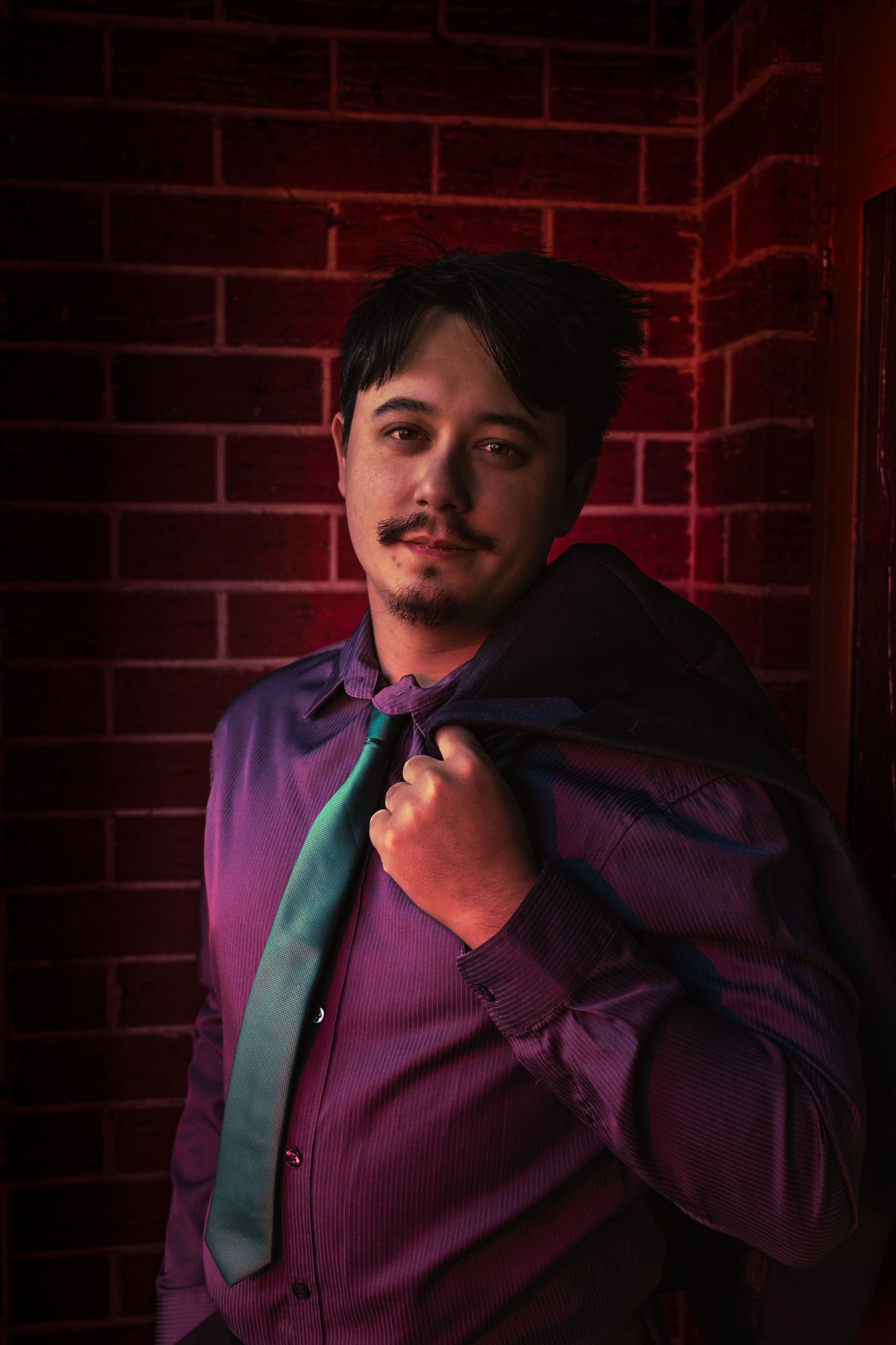 Portrait of a person in a purple jacket against a red neon lit brick wall