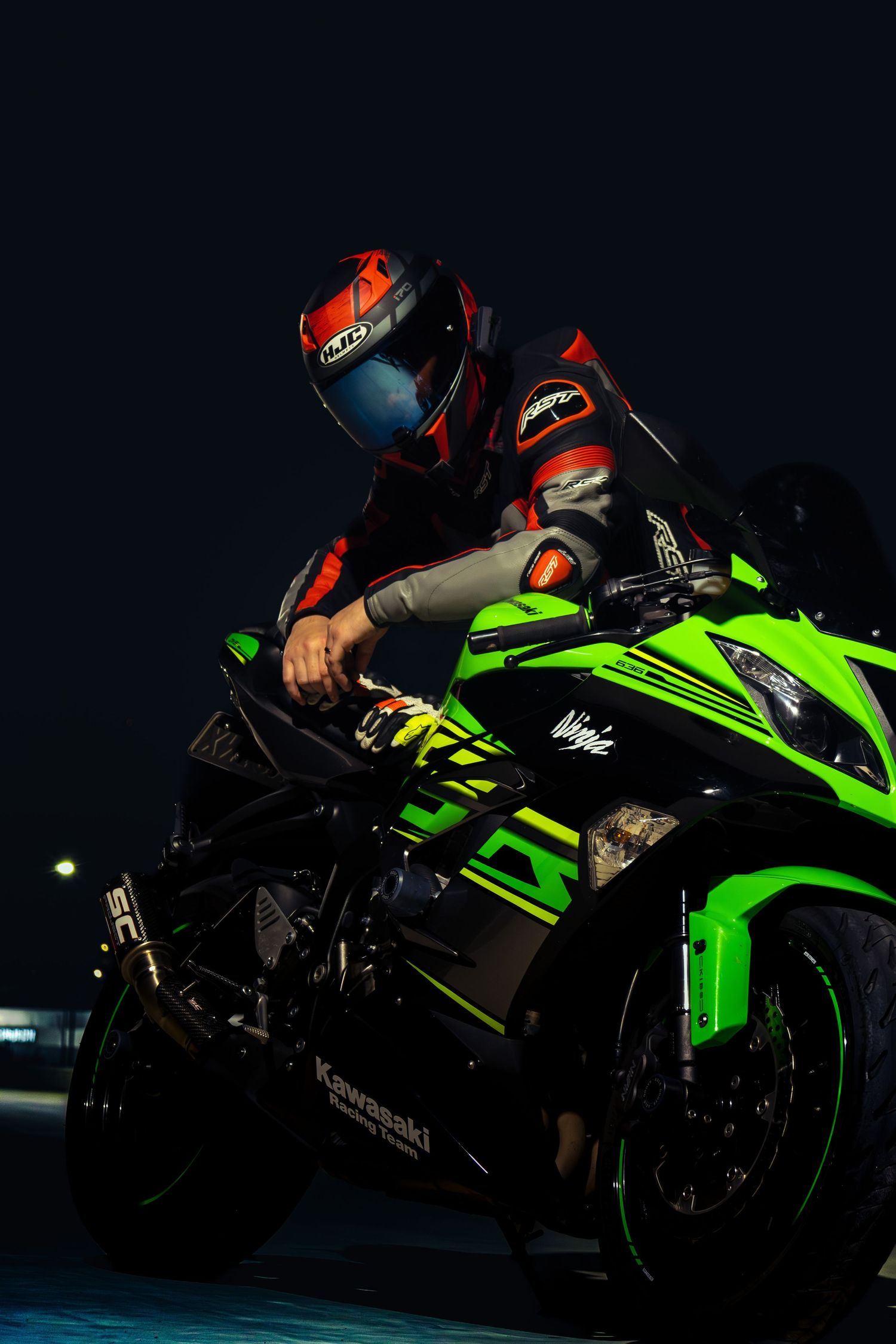 Rider on a green Kawasaki Ninja sportbike lit against a dark background