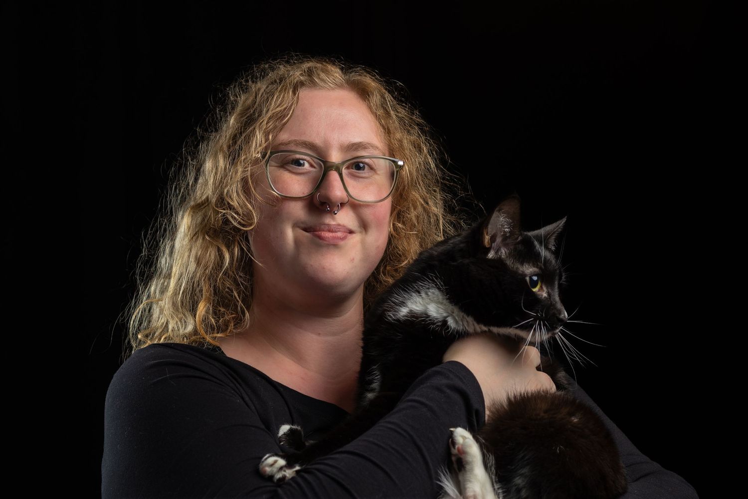 Woman holding her black and white cat in a dark studio portrait