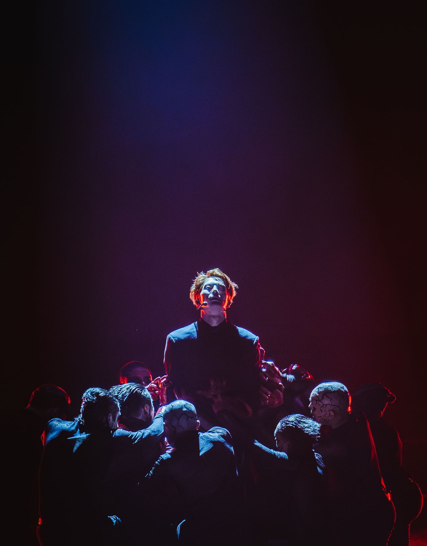 Male performer crowd surfs under dramatic blue and red stage lighting at a live concert.