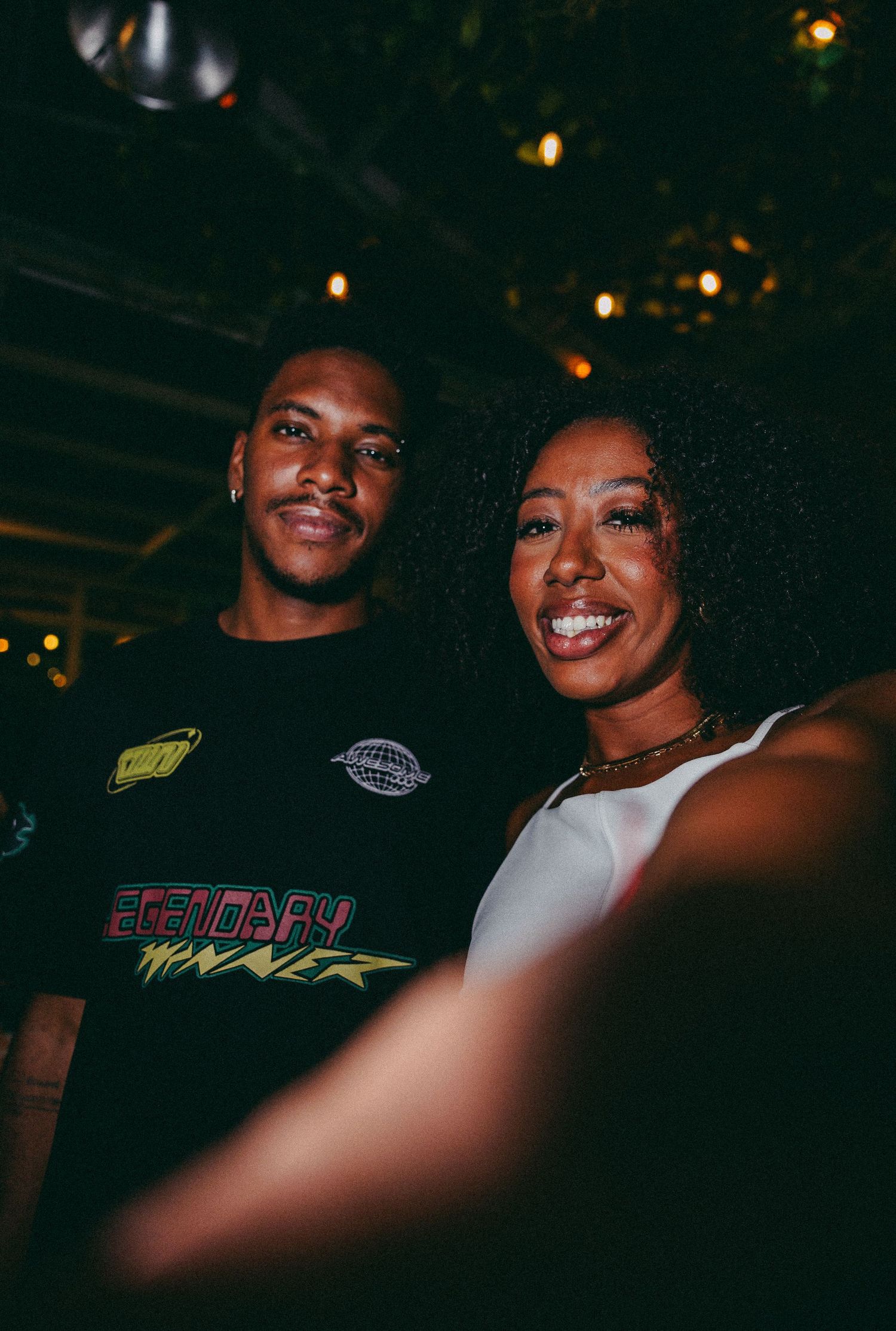 A smiling man and woman pose together for a selfie at a dimly lit music venue event.
