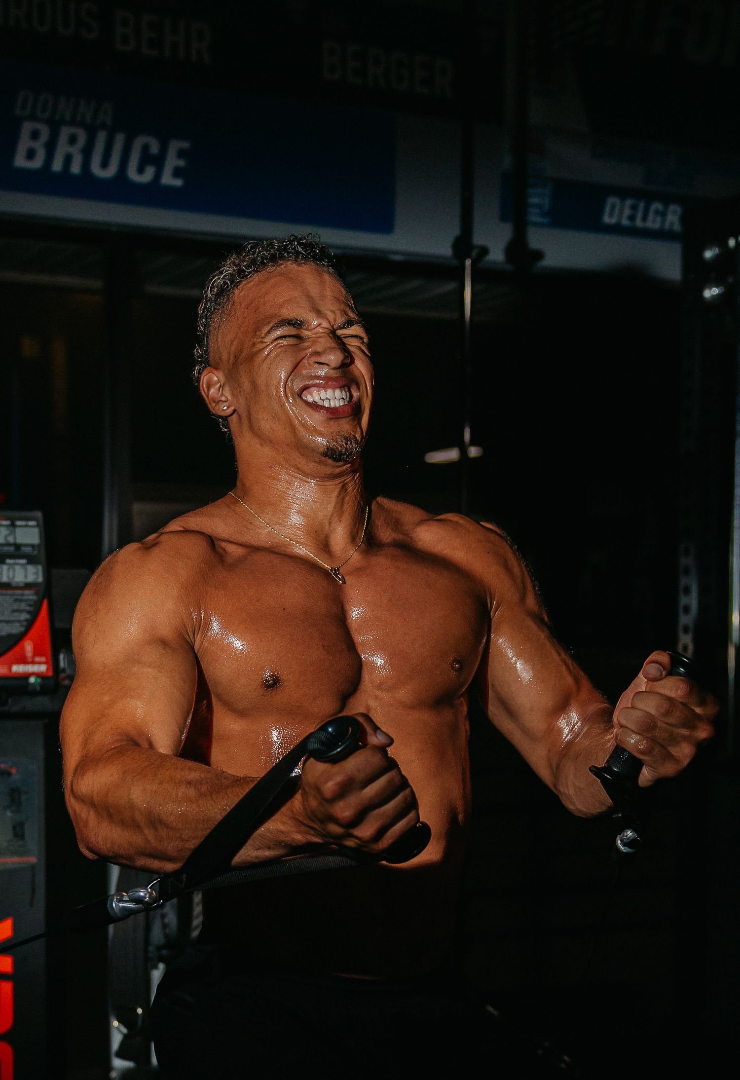 Muscular shirtless man flexing and smiling triumphantly during an intense gym workout session.