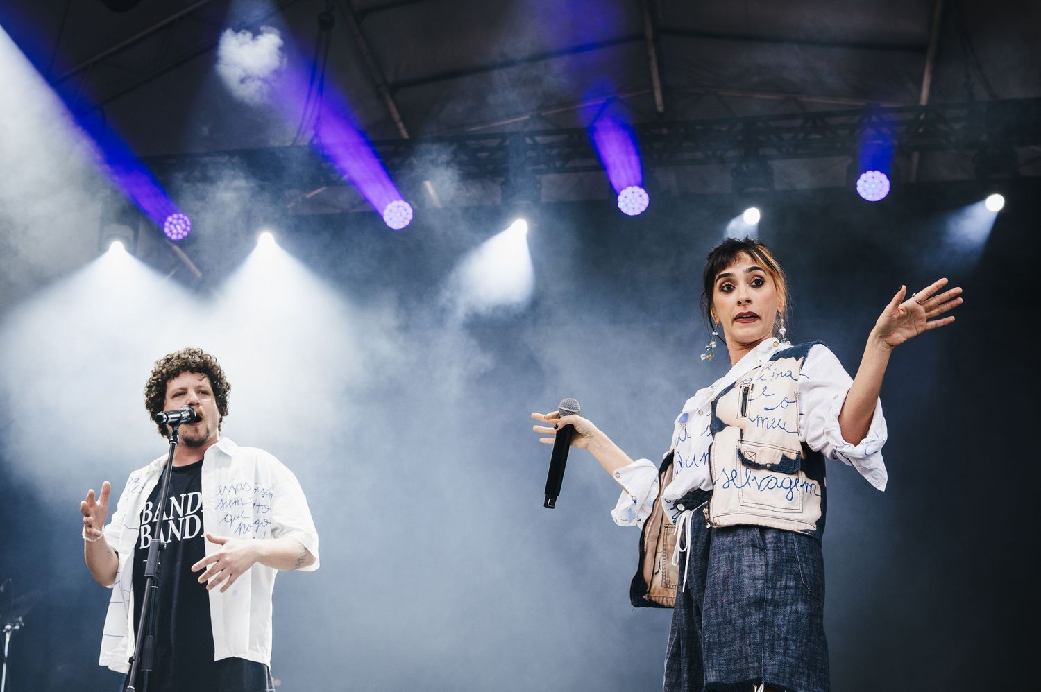 Two performers singing on a smoky concert stage with purple and white stage lights illuminating the night.