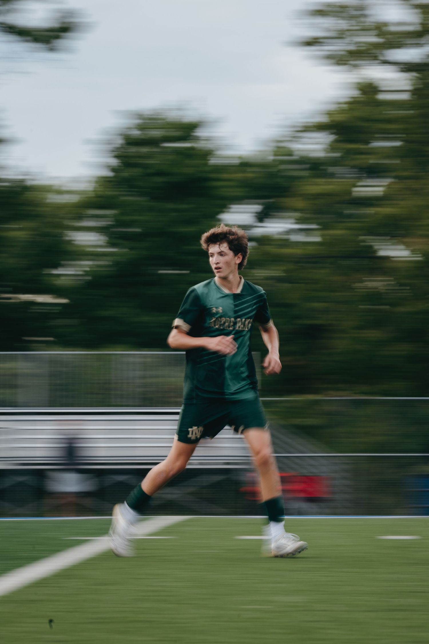 A young soccer player in a green uniform sprints across the field, captured with motion blur effect.