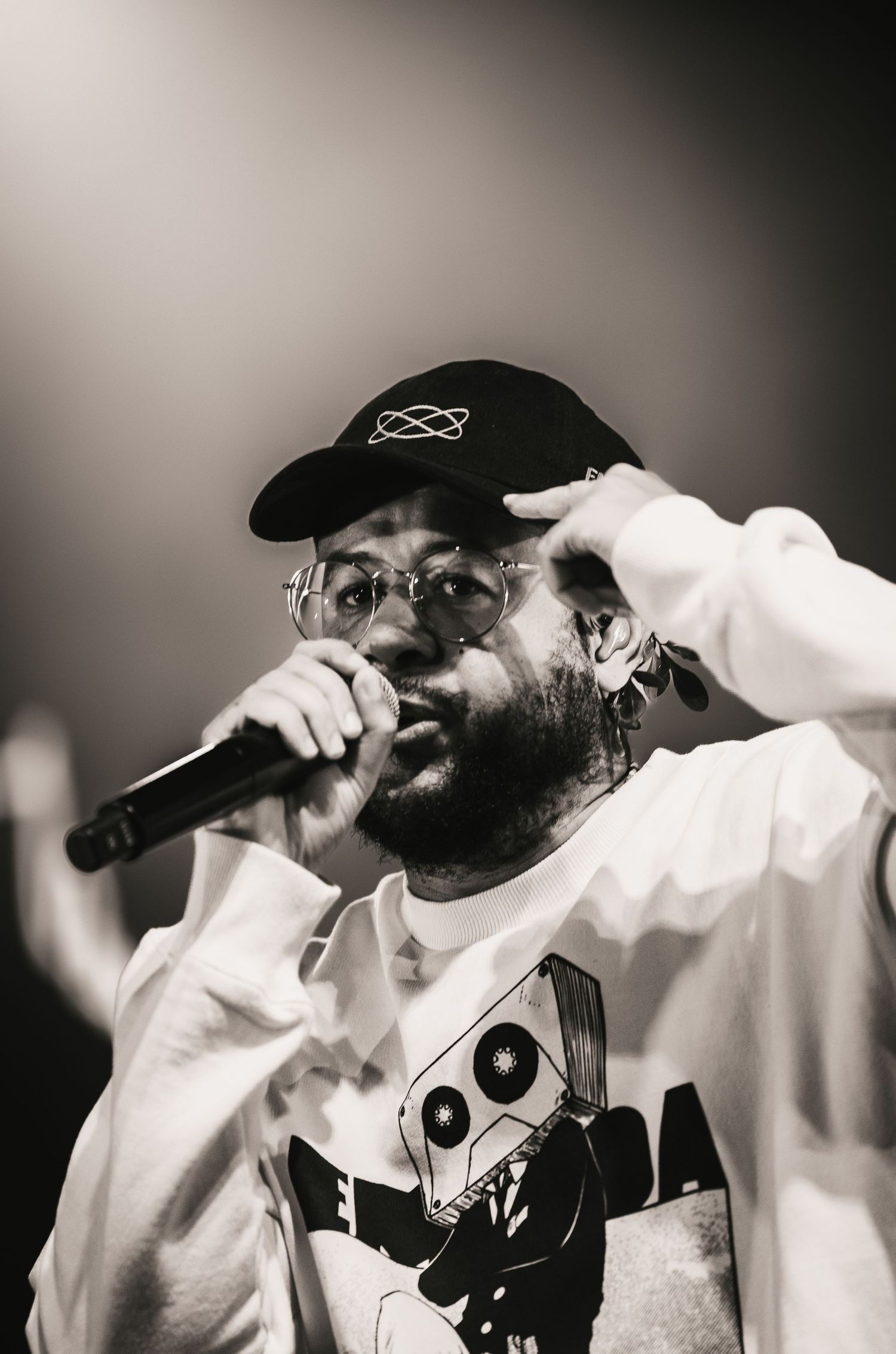 Male rapper in white hoodie and black cap performs with microphone at a live hip-hop concert.